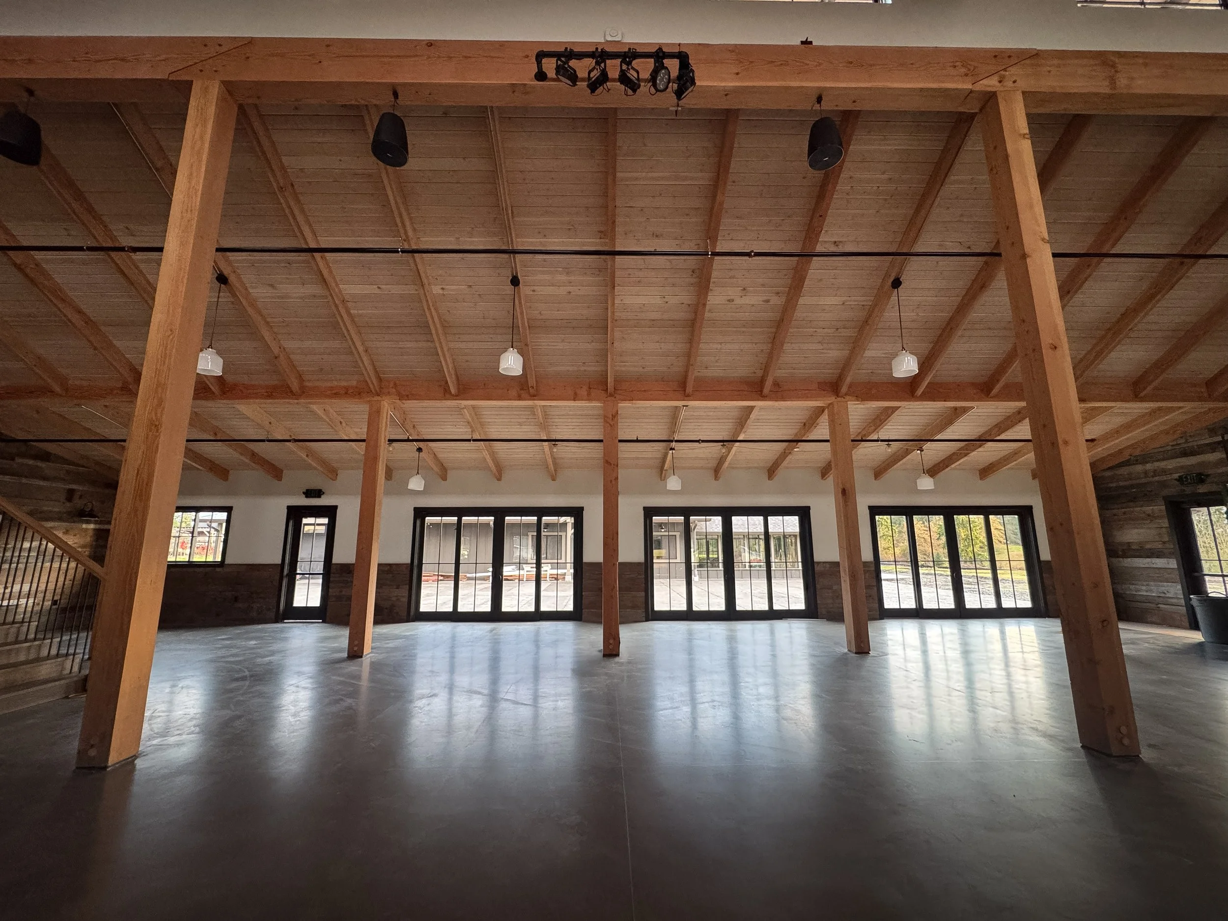 Interior of a building under construction with large windows, wooden ceiling beams, and partially finished walls.