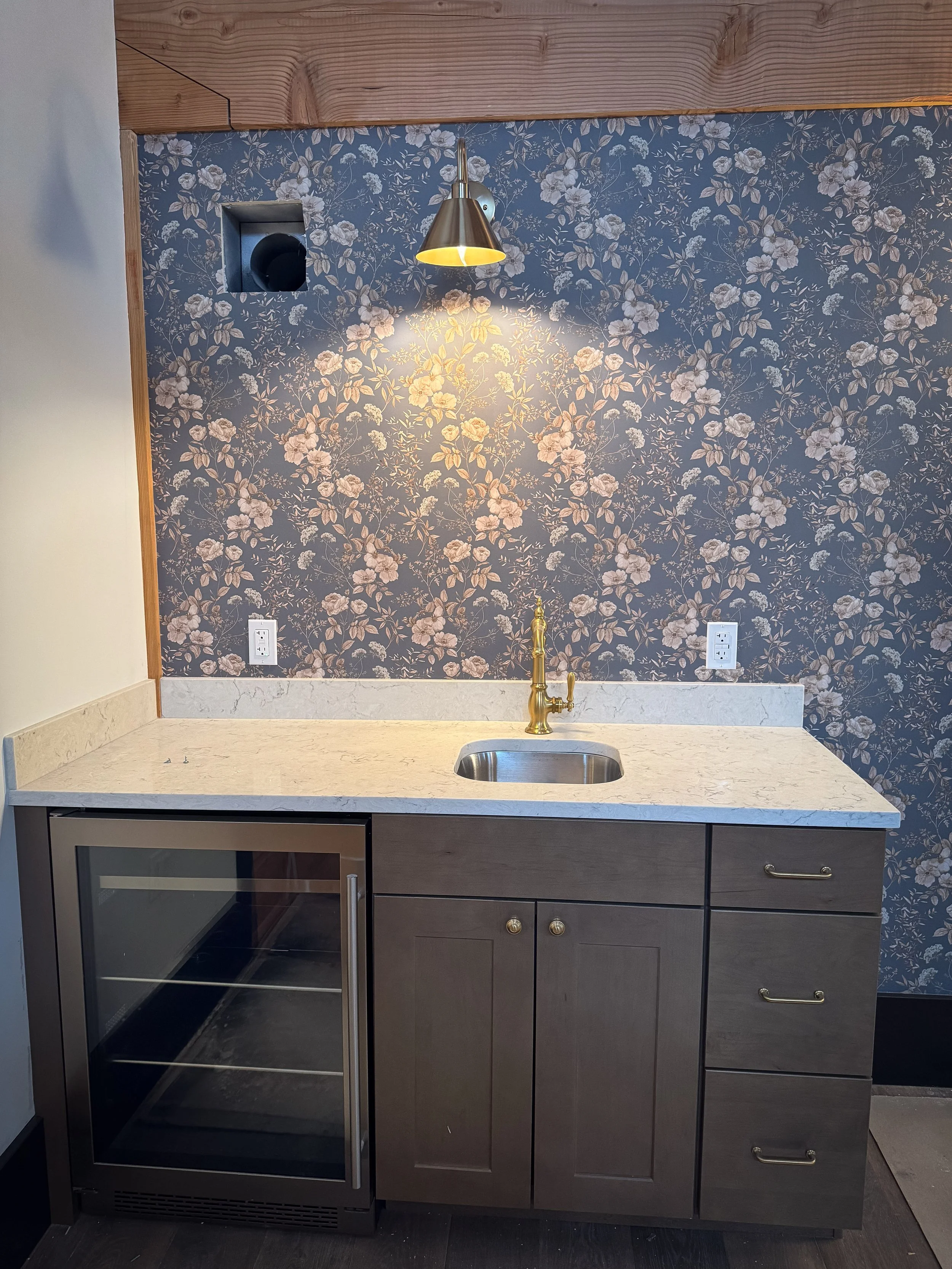 photo of small bar with a sink, mini fridge and cabinets with gold light above