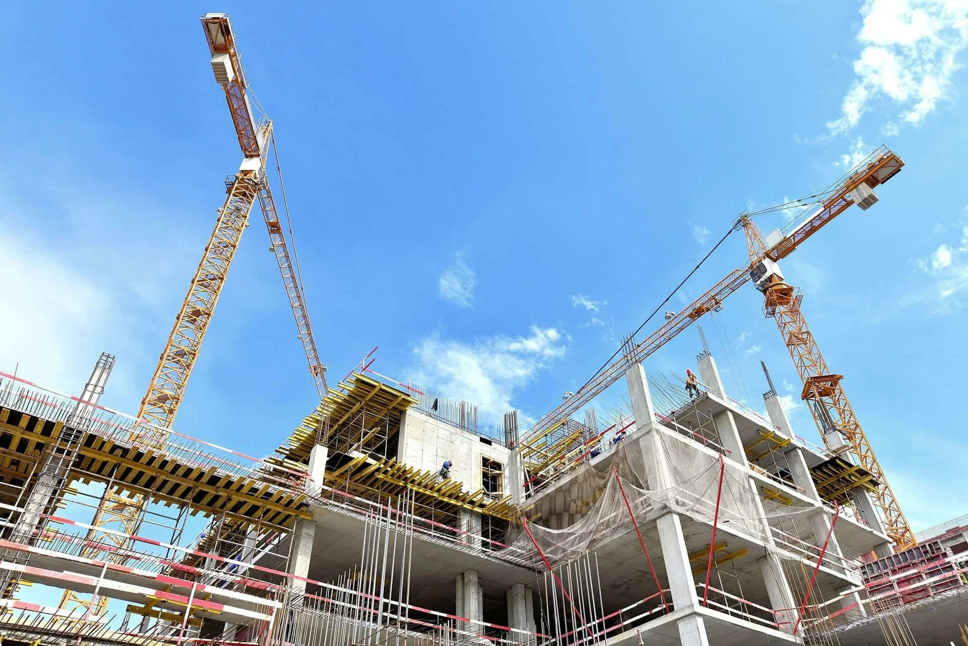 Construction site with cranes and building framework under blue sky.