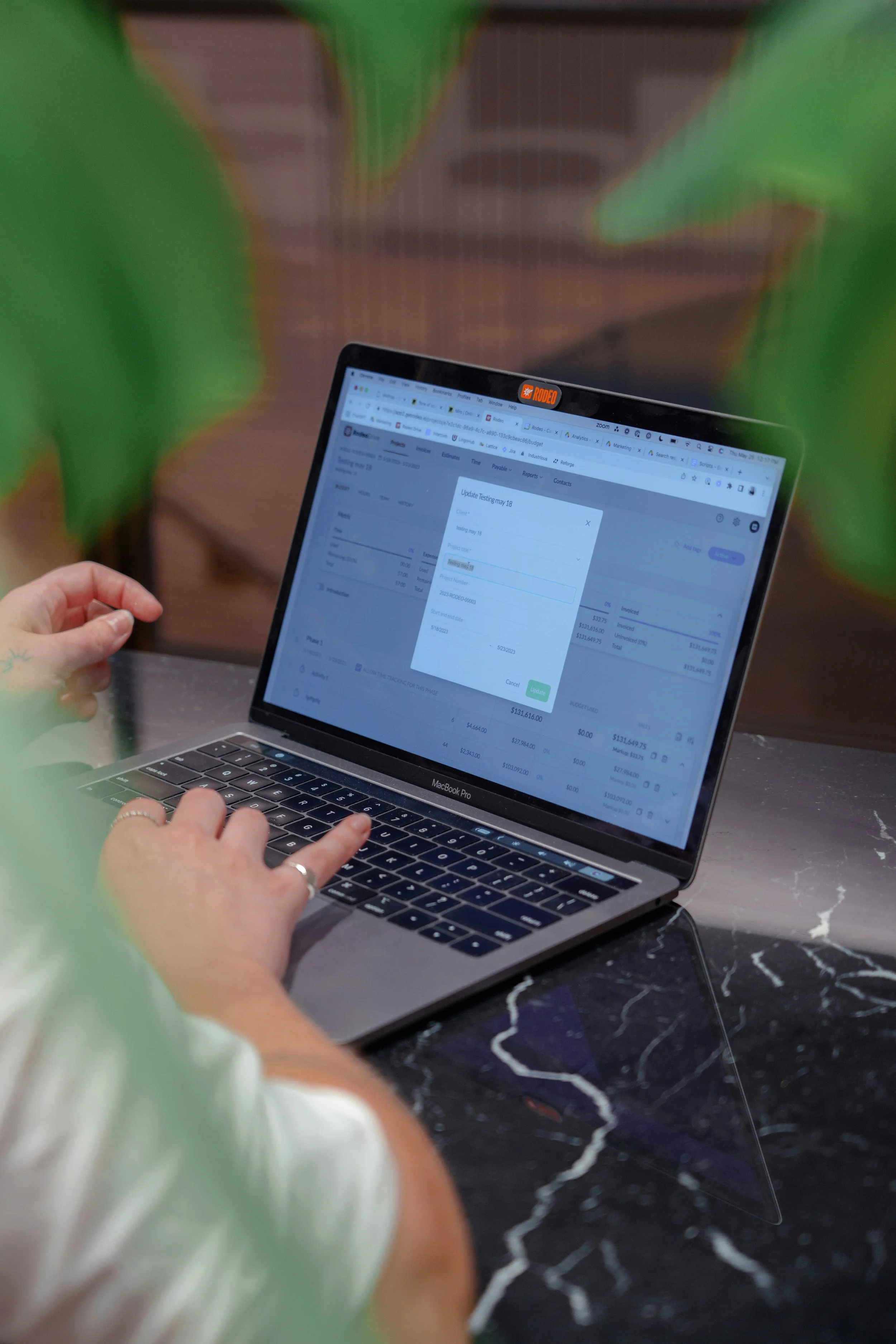 Person using a MacBook Pro on a black marble table with a plant in the foreground.