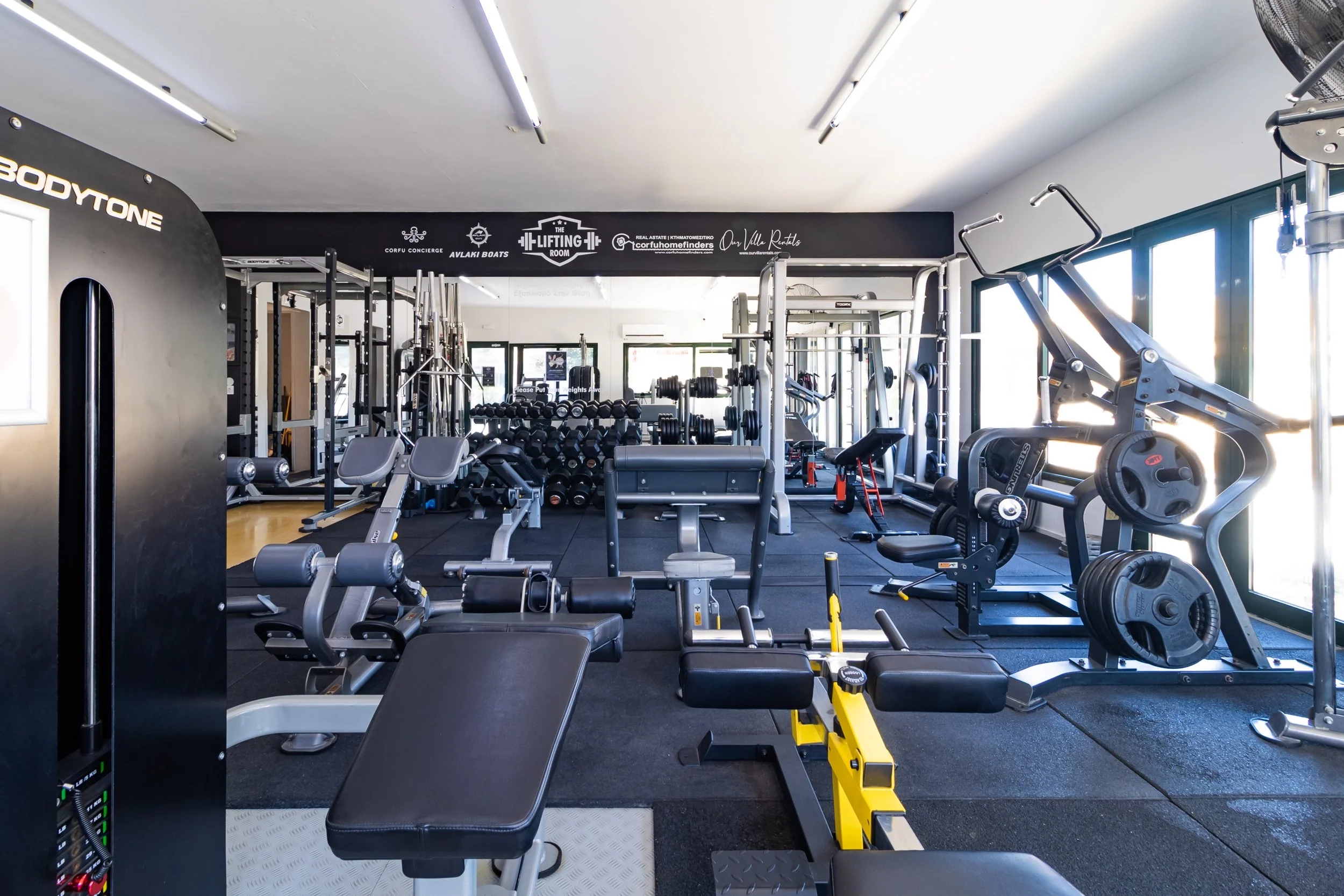 Modern gym interior with various workout equipment, including weight machines, benches, and dumbbells.