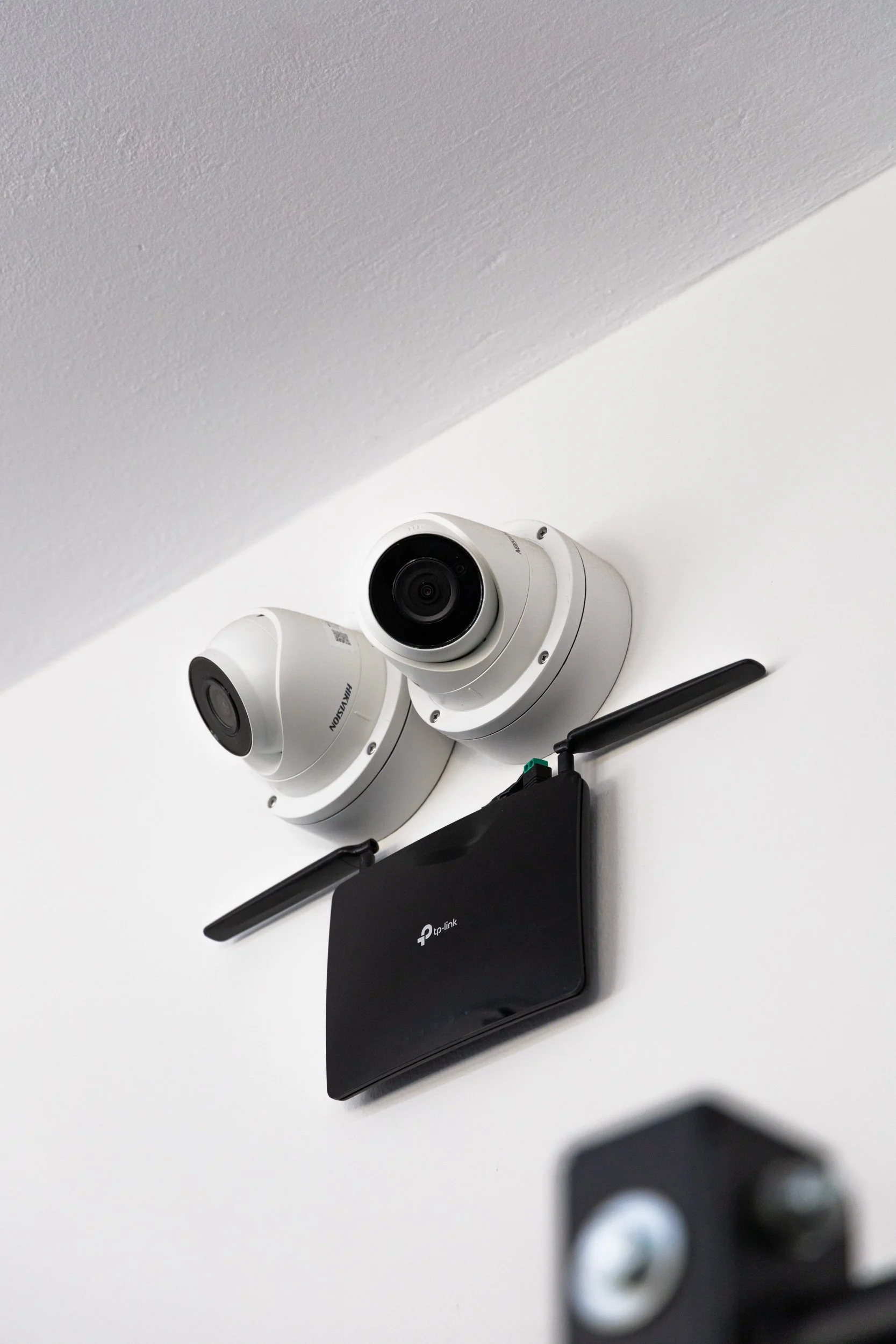 Security cameras mounted on a white wall above a TP-Link router with antennas.