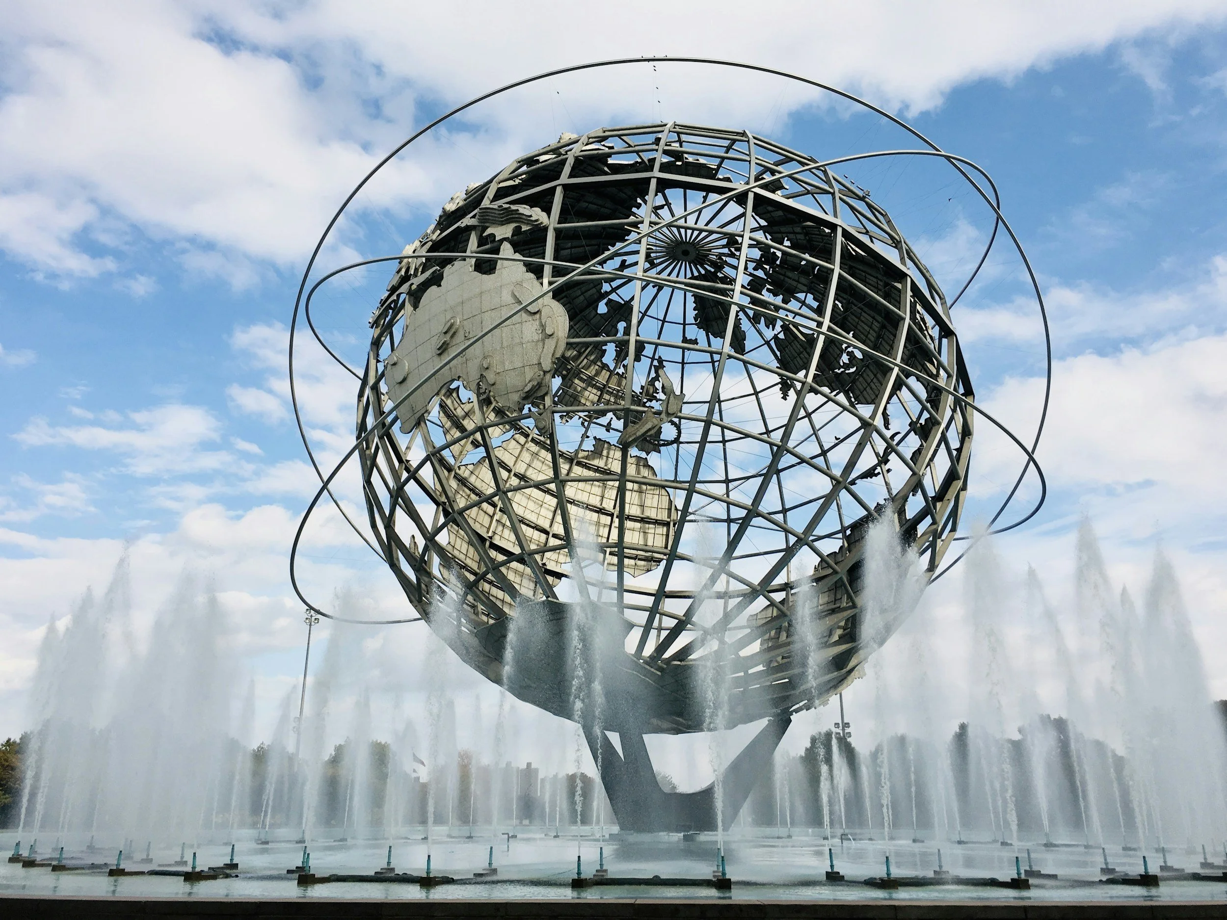 The Unisphere, a large metal globe sculpture with water fountains surrounding it, against a partly cloudy sky.