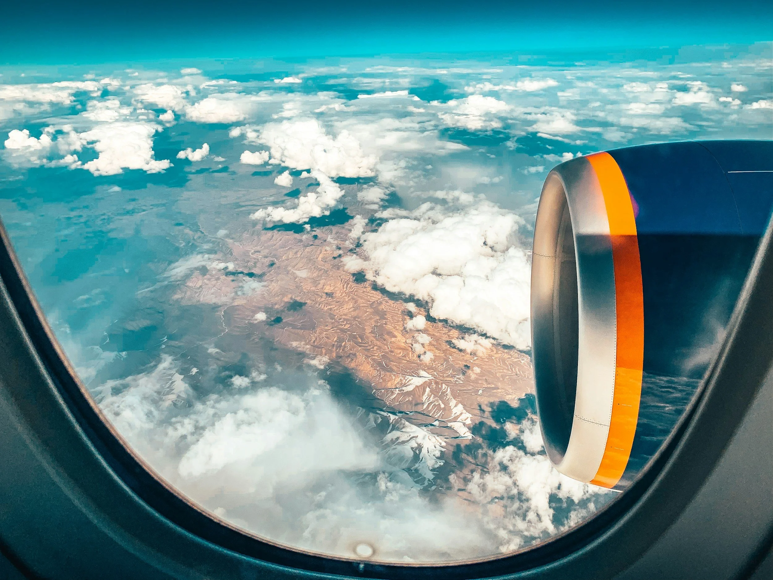 View from airplane window showing clouds, mountain terrain, and part of an airplane engine.