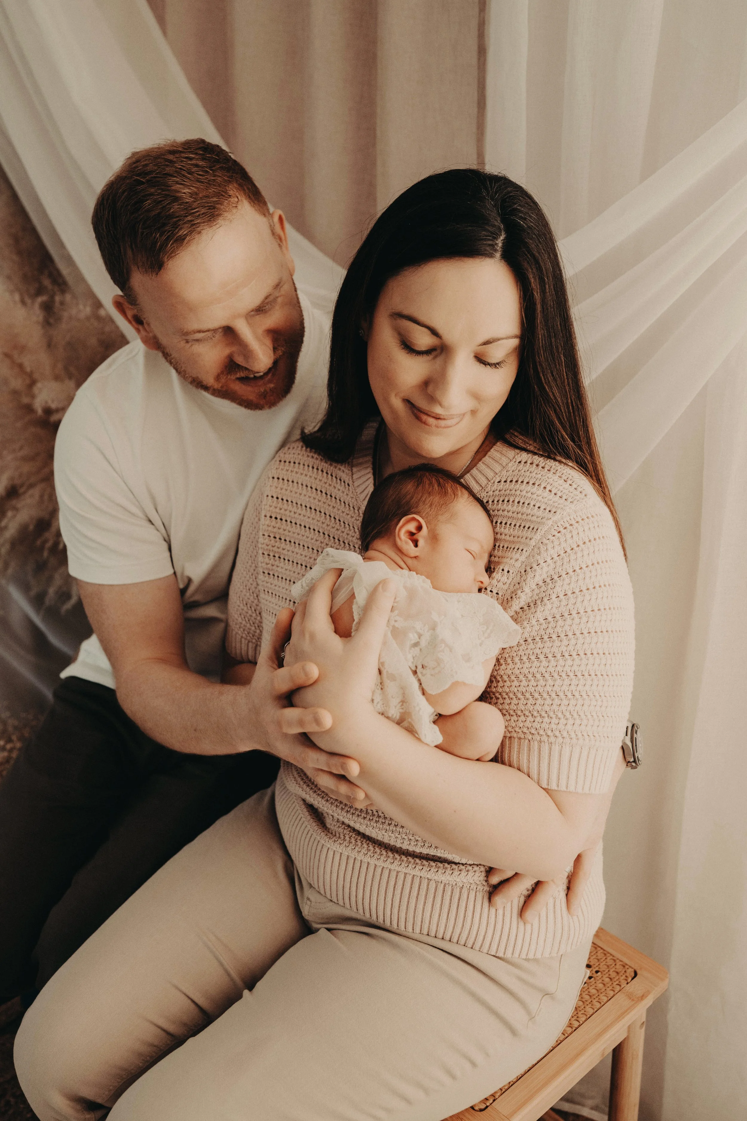 mother with dark hair and father with red hair and cuddling their newborn baby girl