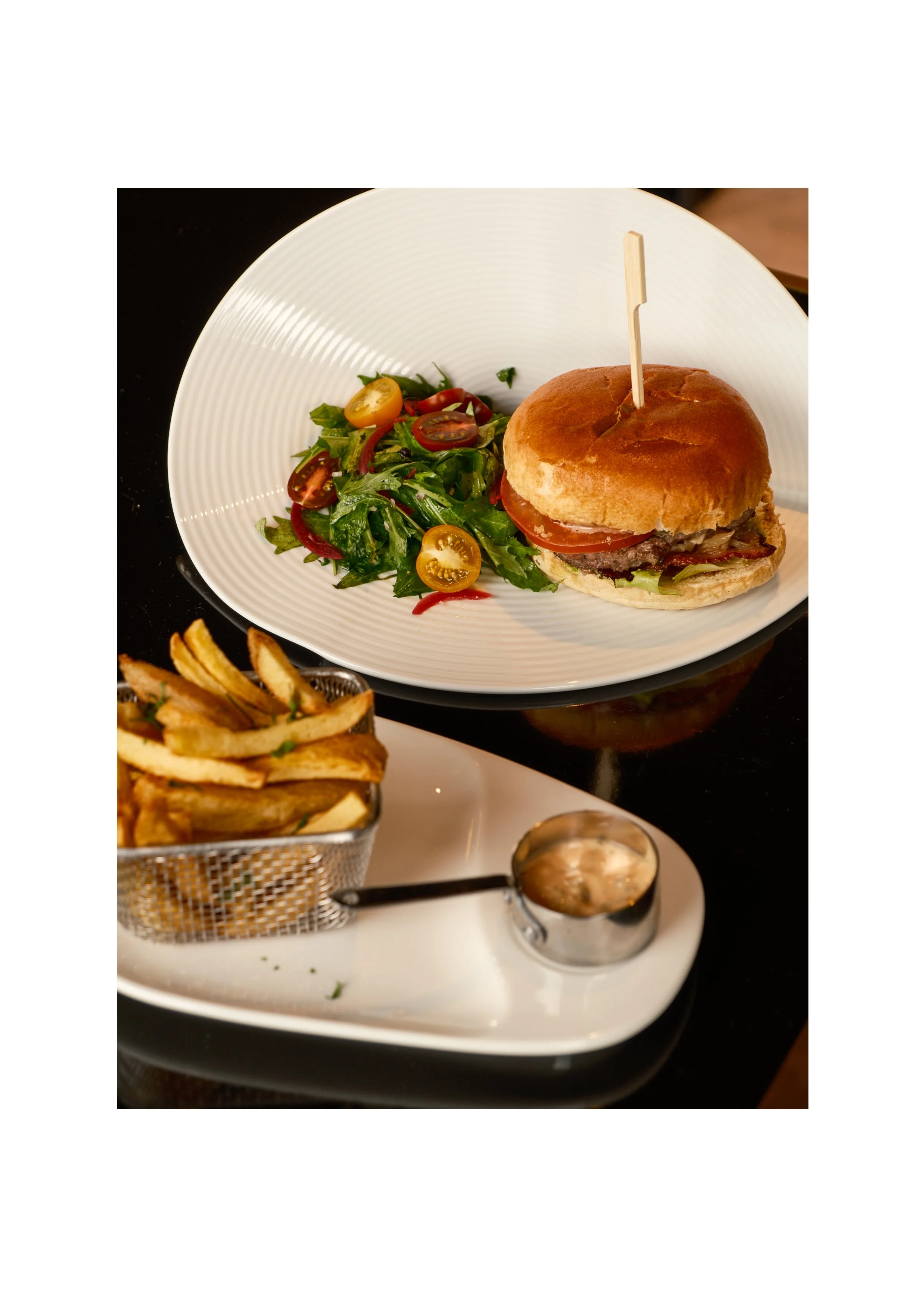 Gourmet burger and crispy fries served on a sleek black table, professional hotel restaurant menu photography.