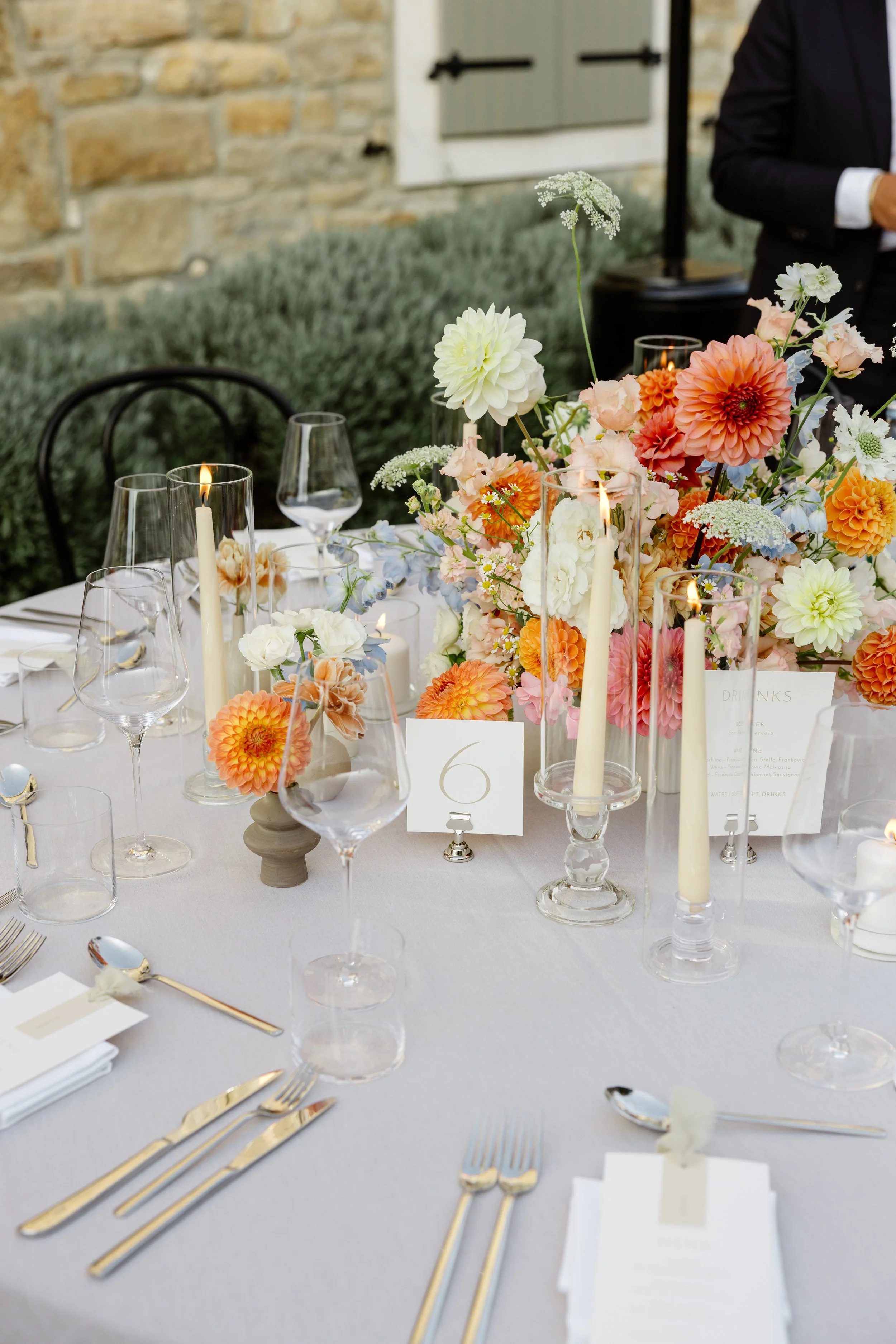 Decorated table with floral centerpiece, candles, glassware, and utensils for a formal event.