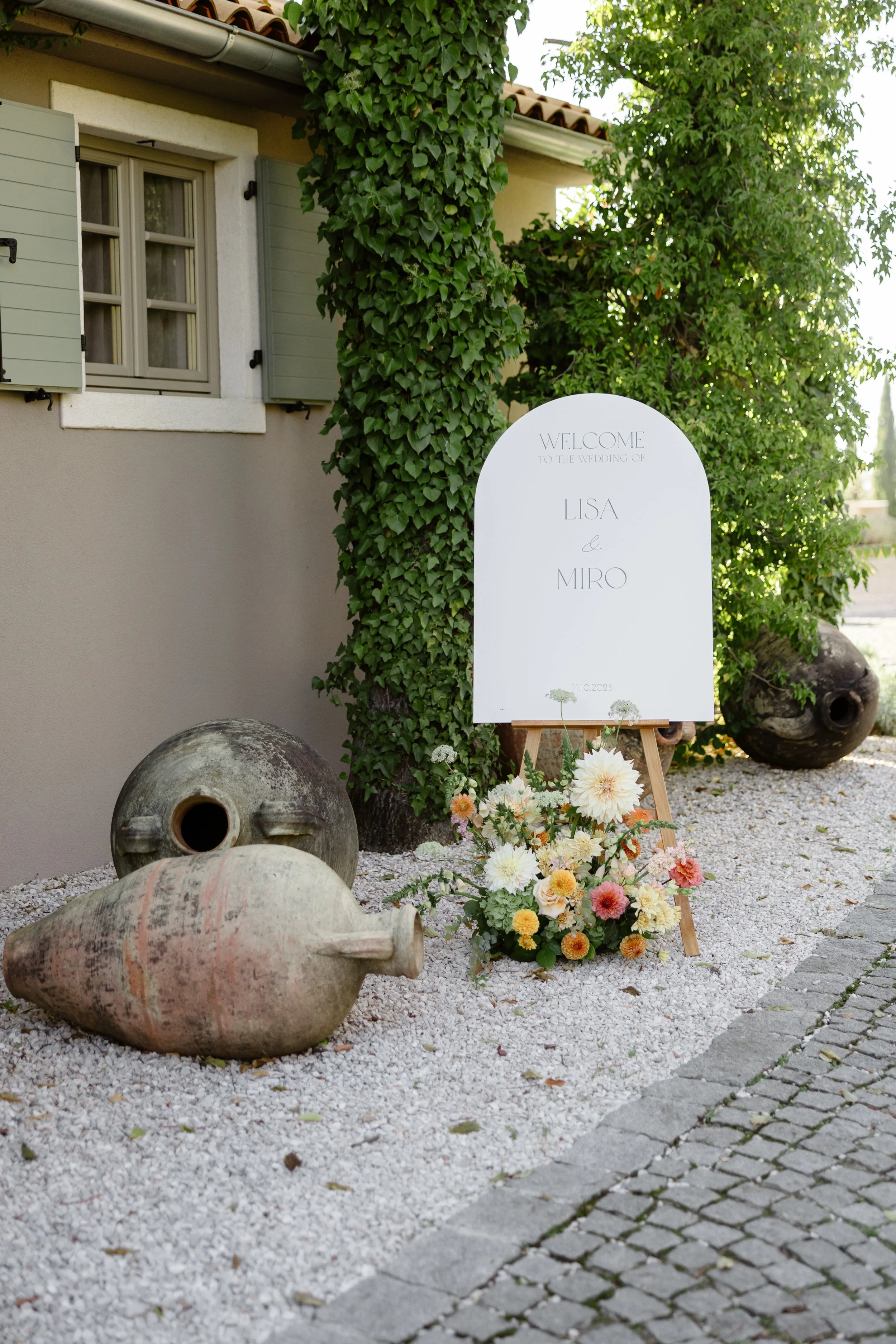 Wedding welcome sign with flowers and vintage pottery outside a house