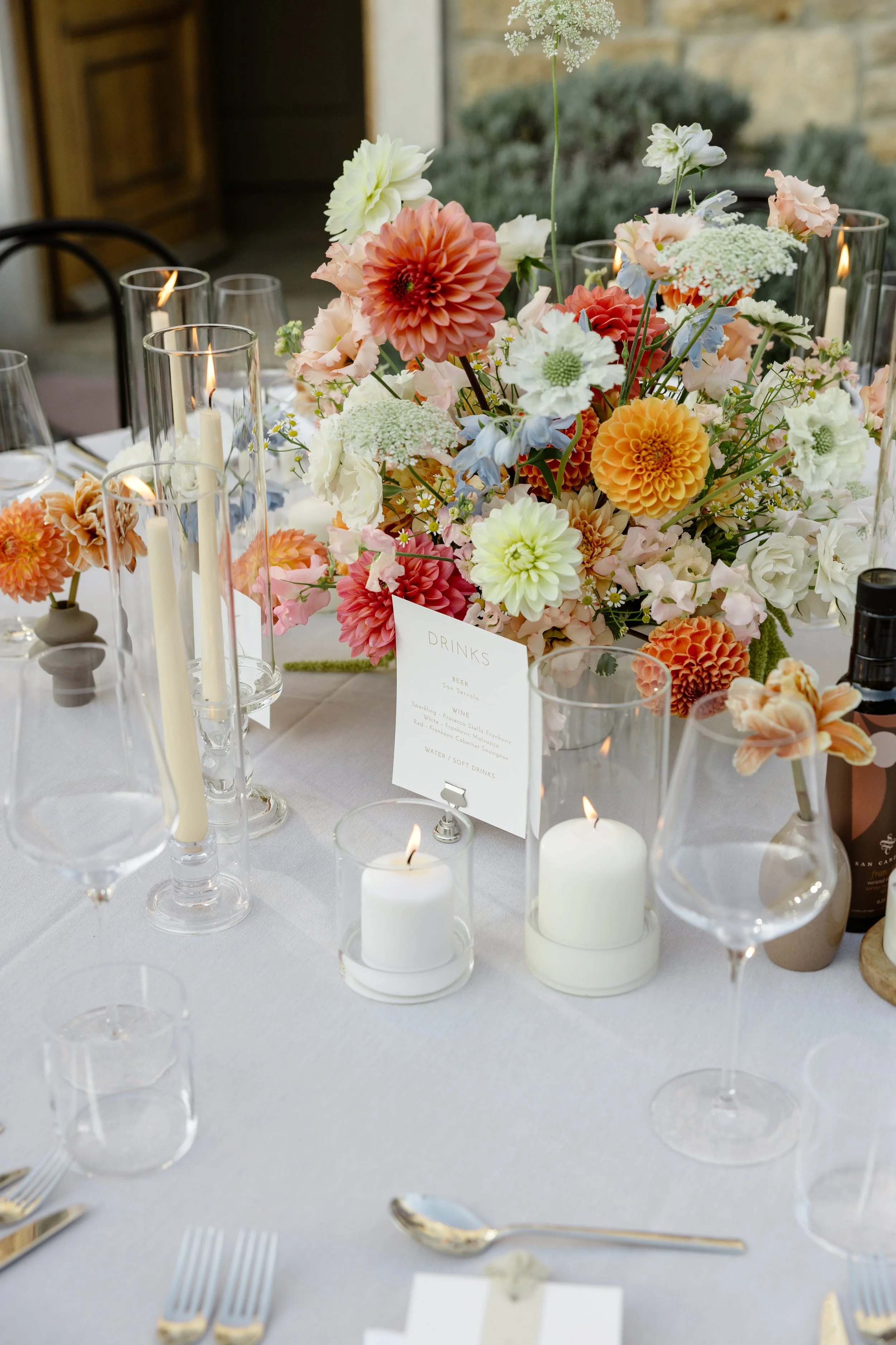 A floral centerpiece featuring various pastel-colored flowers on a decorated dining table with candles and glassware.