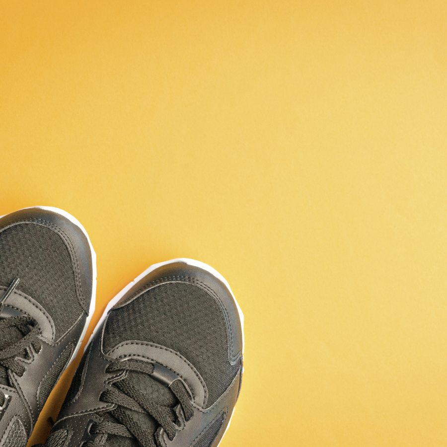 Close-up of black athletic shoes with gray accents on a yellow background.