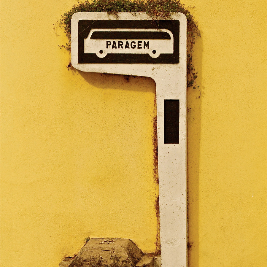 A white and black parking sign shaped like a key with the word 'PARAGEM' in the top section, mounted on a yellow wall.