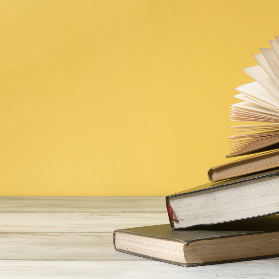 Stack of books on a wooden surface with a yellow background, one book open with pages fanned out.