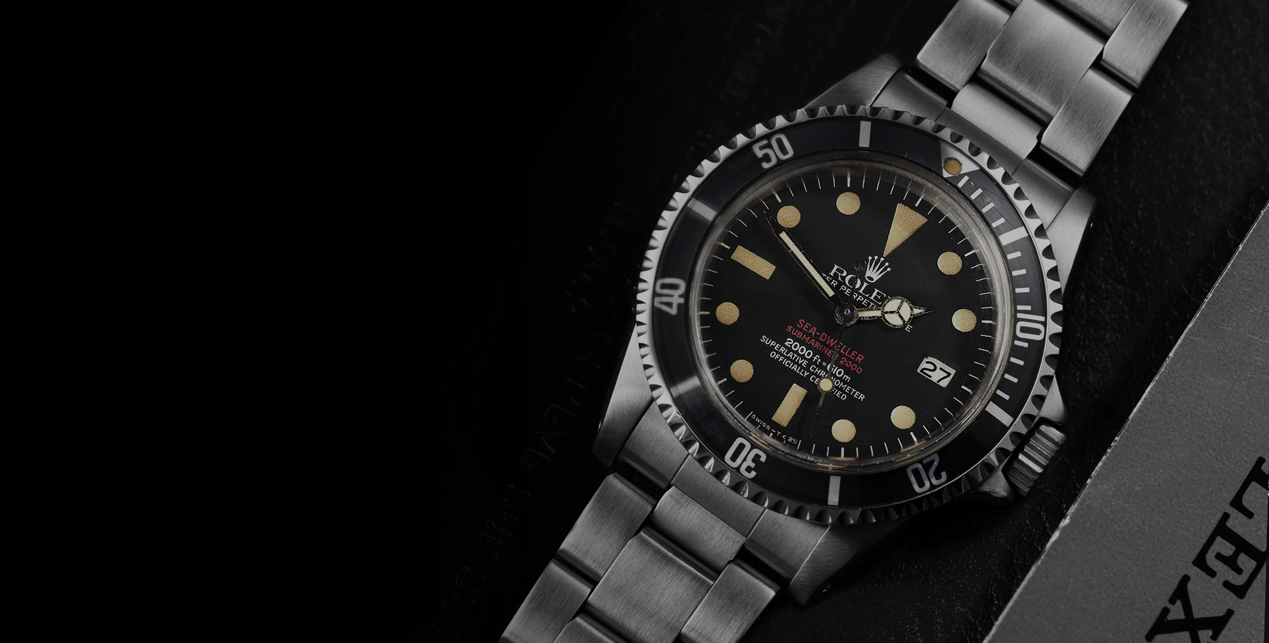 Montre Rolex Submariner Sea-Dweller avec un cadran noir, indicateurs lumineux, bracelet en acier, affichant la date, posé sur un fond noir.