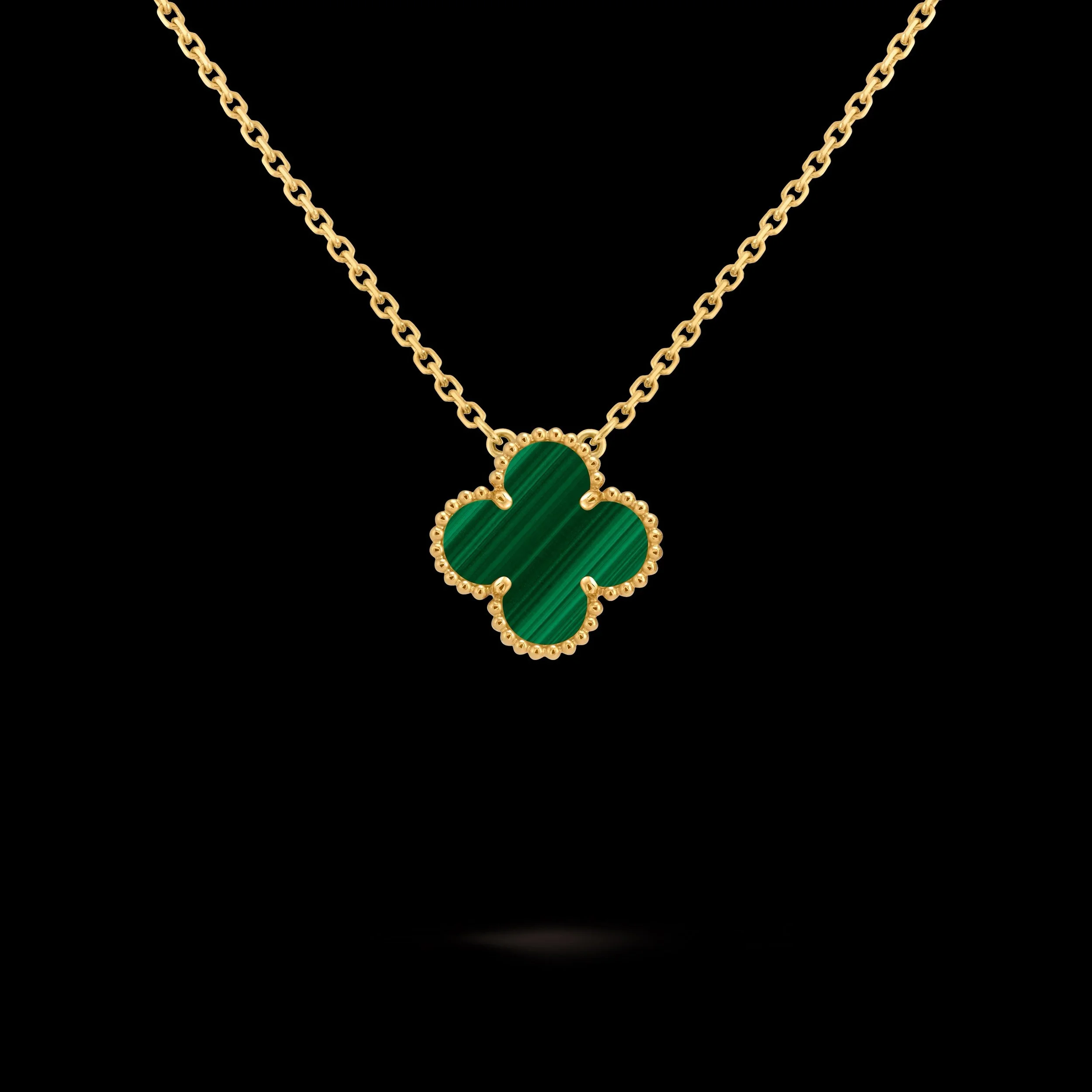 Collier avec pendentif en forme de trèfle à quatre feuilles en or avec pierre verte, posé contre un fond noir.