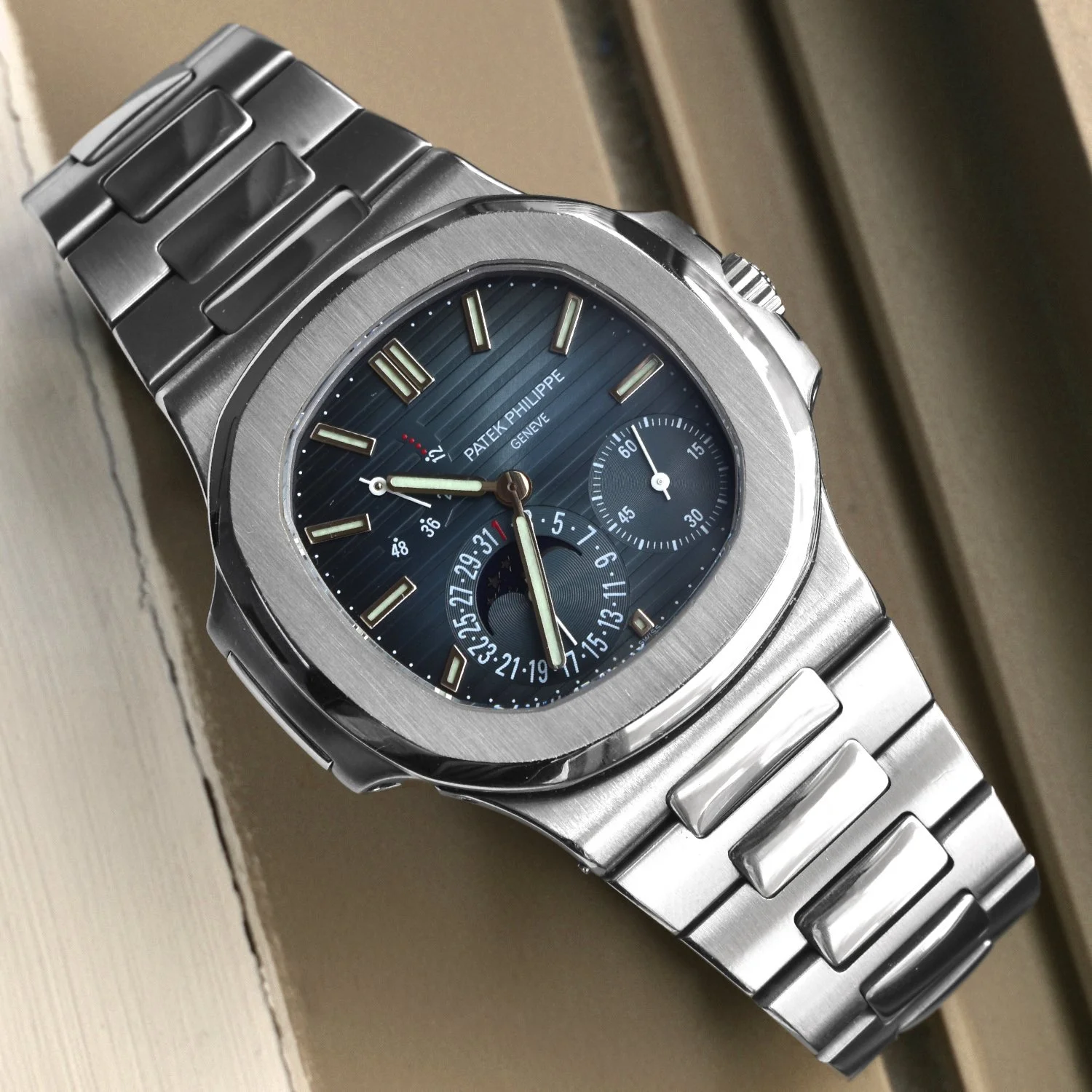 Montre en acier inoxydable avec un cadran bleu et trois sous-cadrans, marque Patek Philippe, bracelet métallique.