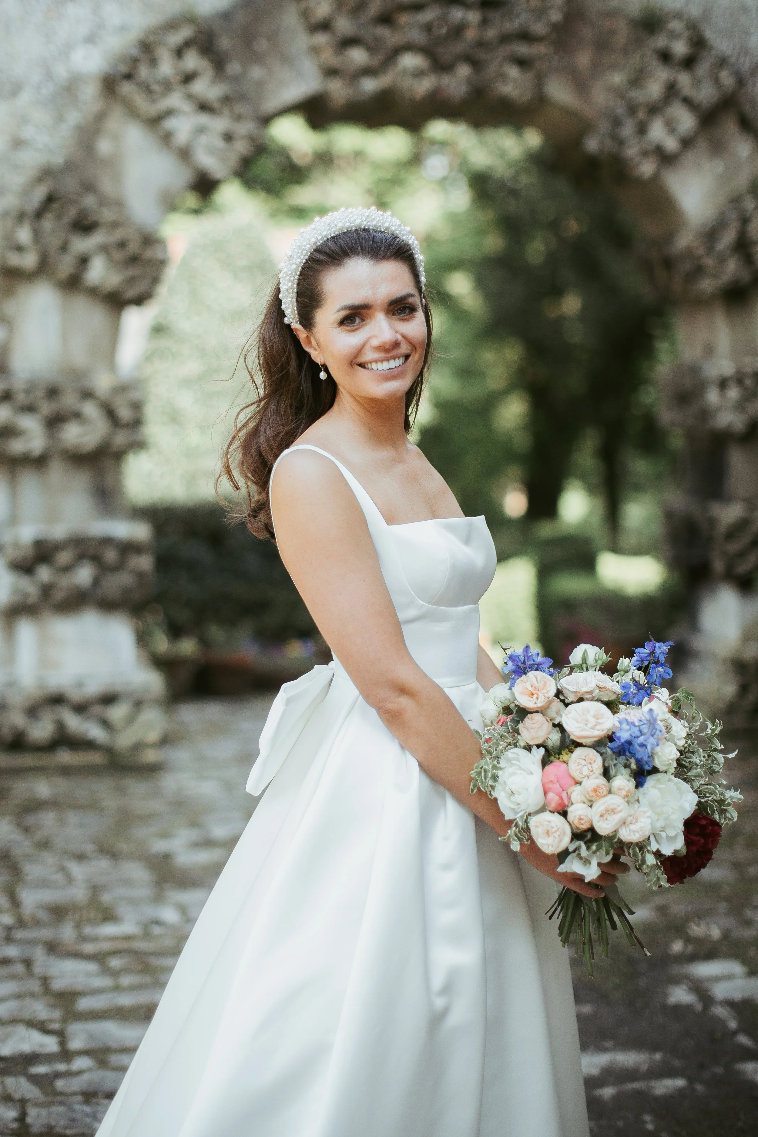 Bride in white dress holding colorful bouquet in outdoor setting.