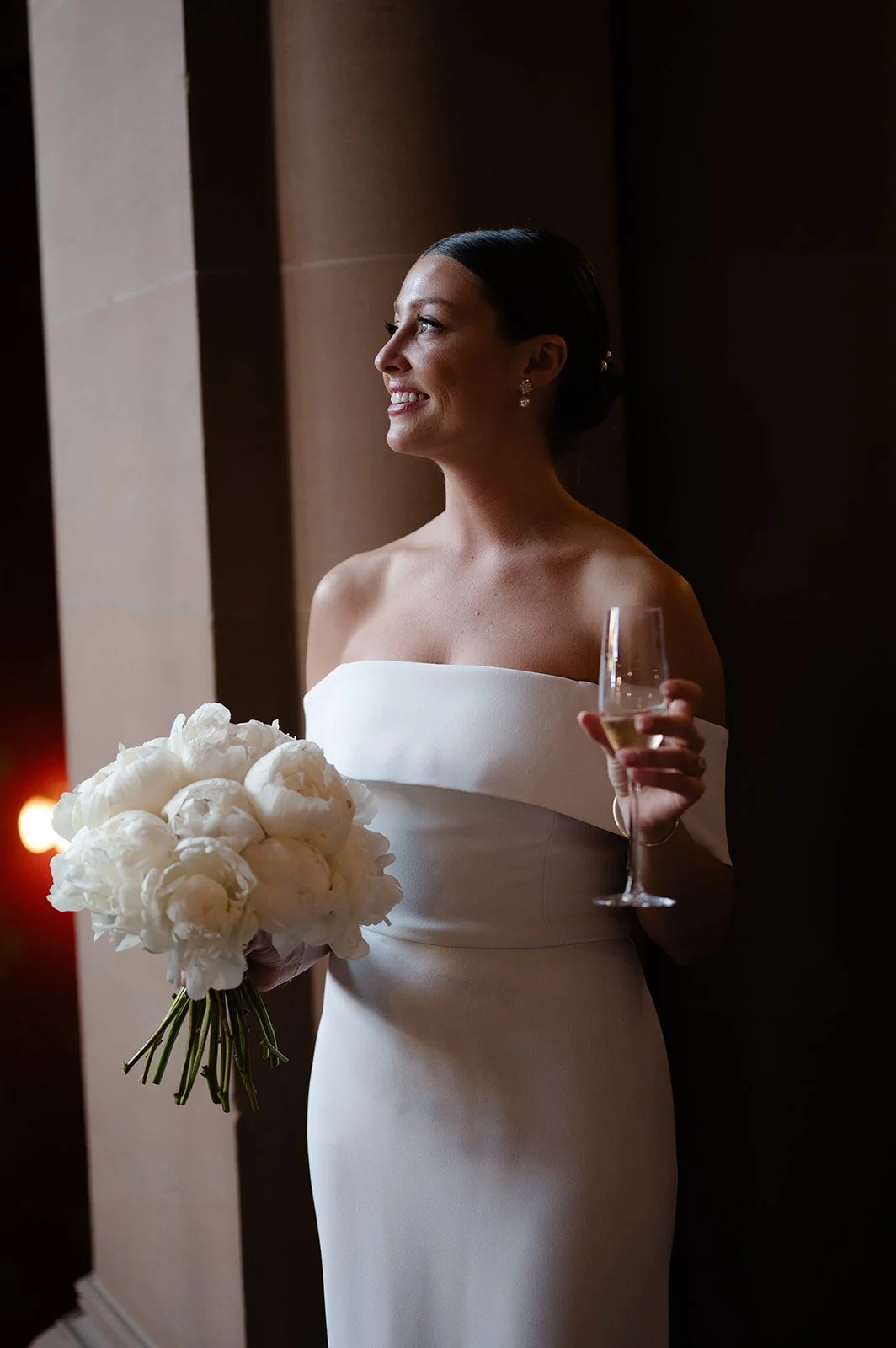 Bride in white dress holding bouquet and champagne glass, smiling.