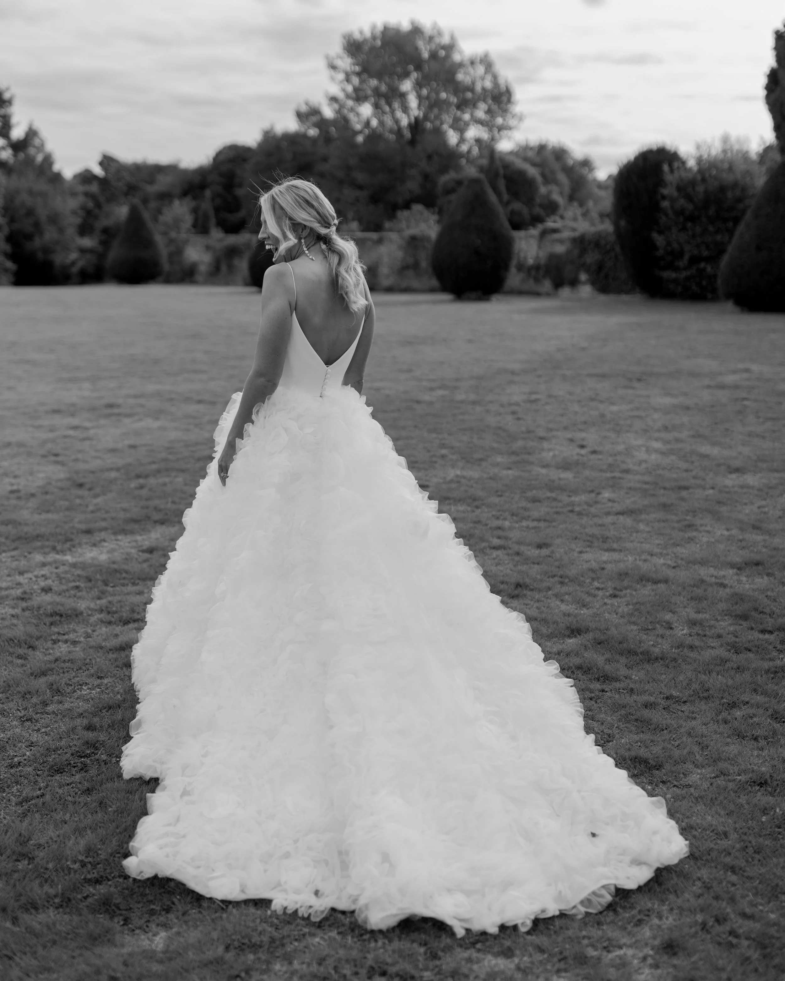 Woman in wedding dress walking on grassy field, black and white photo