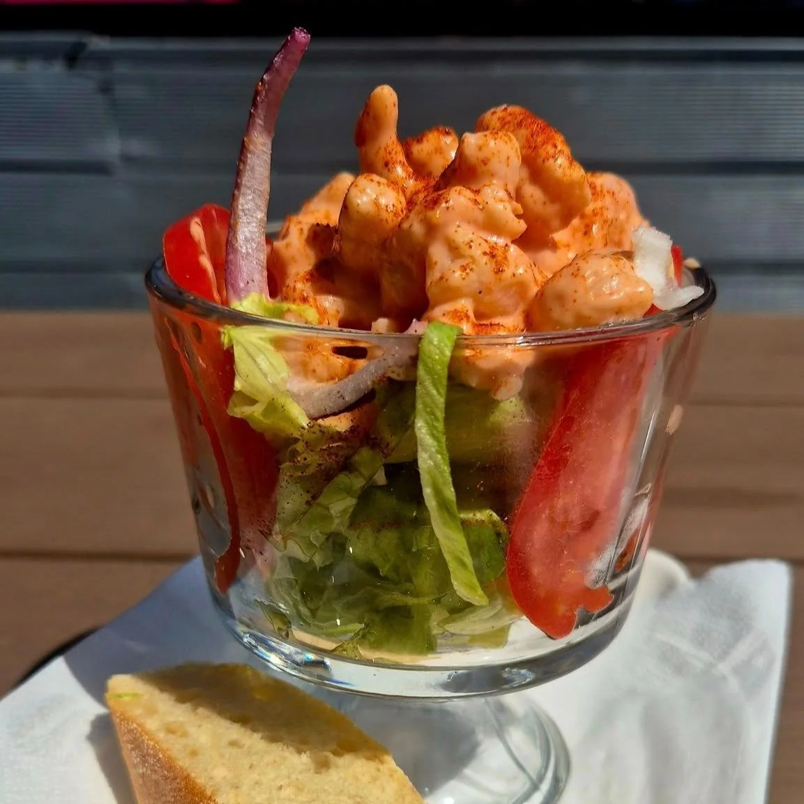 Shrimp salad in a glass with lettuce, tomato, red onion, served with a slice of bread.