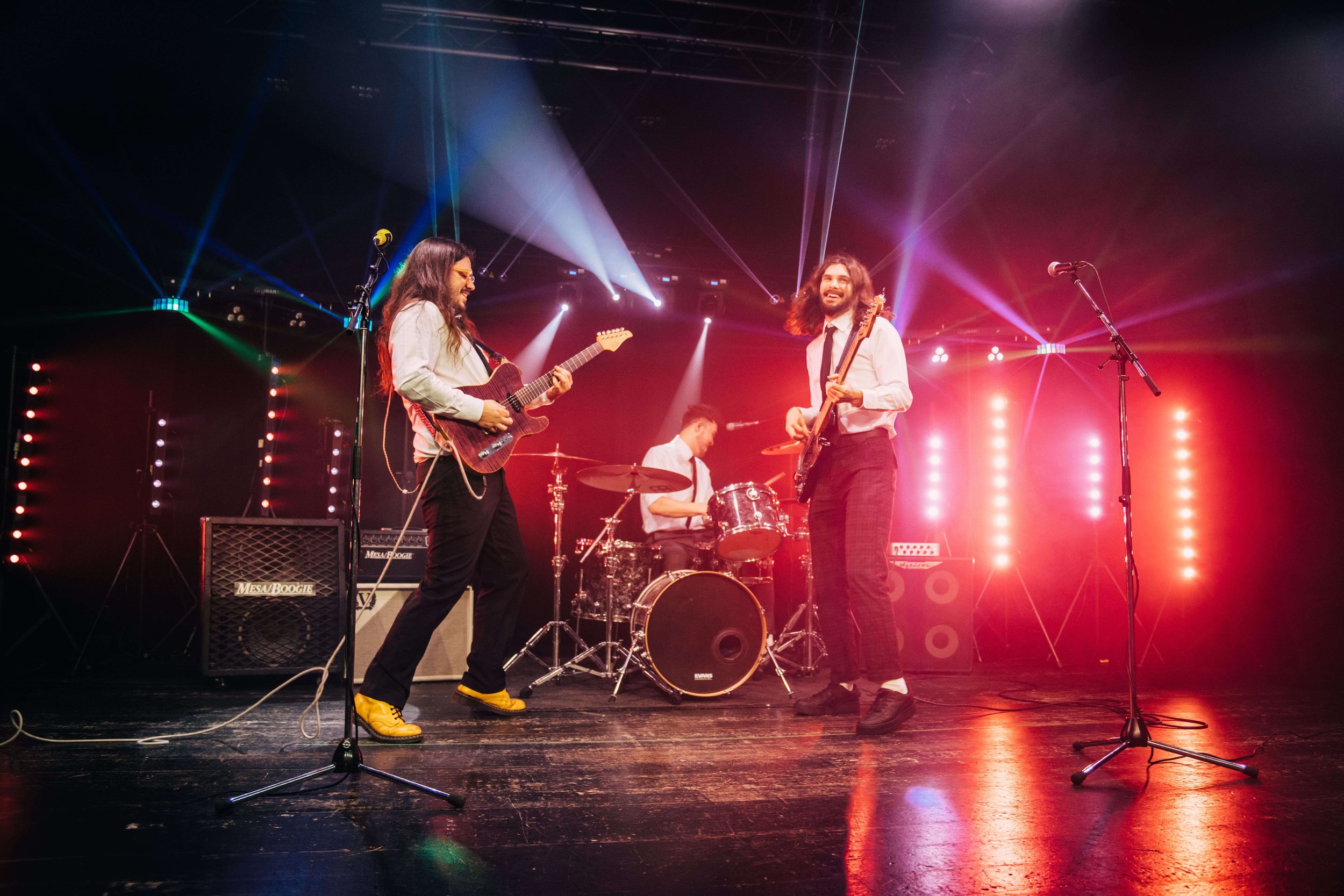 Musicians performing on stage with colorful lights and instruments, including guitars and a drum set.