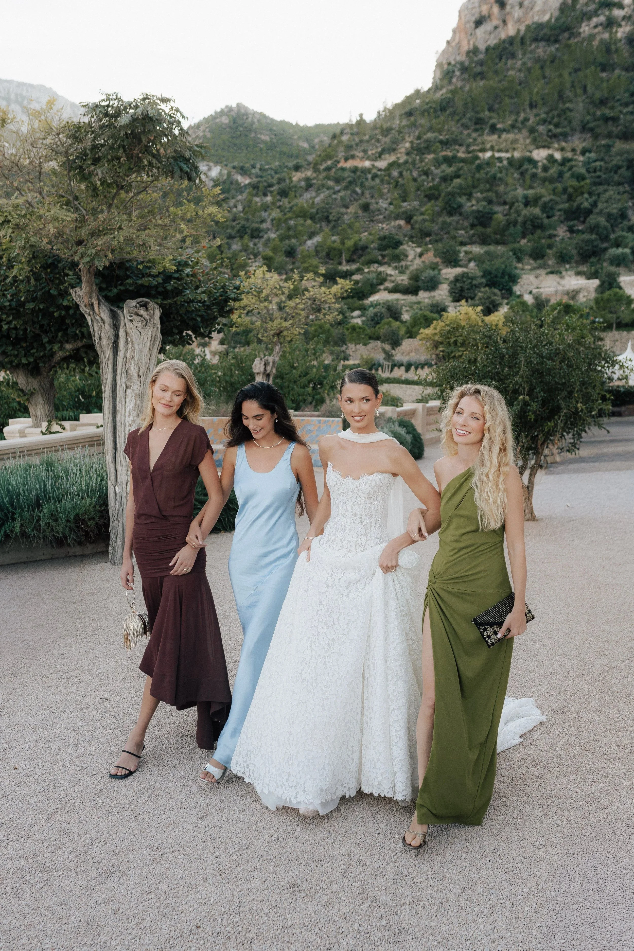 Vier Frauen in eleganten Kleidern bei einem Outdoor-Event vor einer landschaftlichen Kulisse mit Bäumen und Bergen.