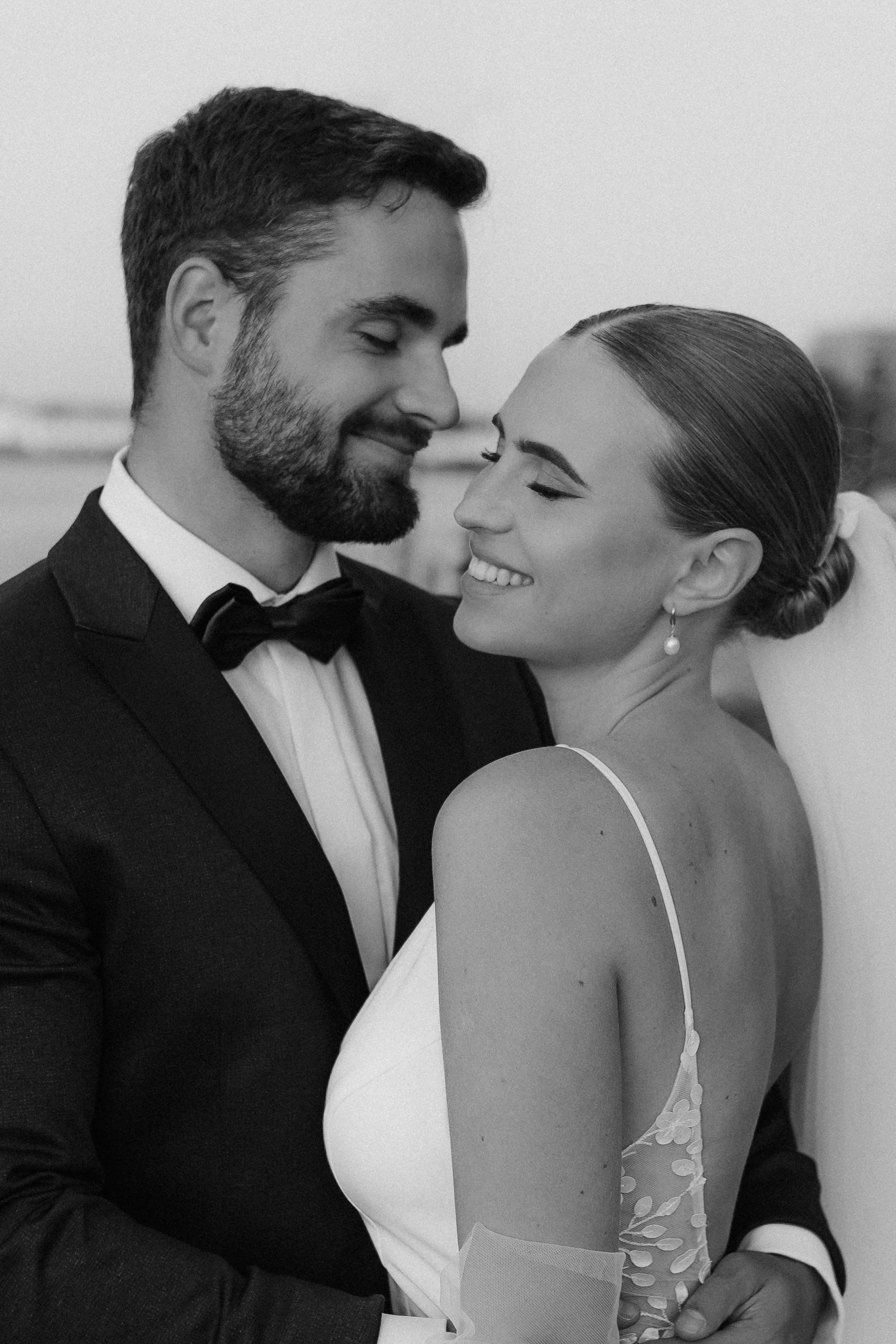 Ein glückliches Paar in formeller Kleidung, umarmt sich liebevoll auf einer Hochzeit im Freien, Schwarz-Weiß-Foto.