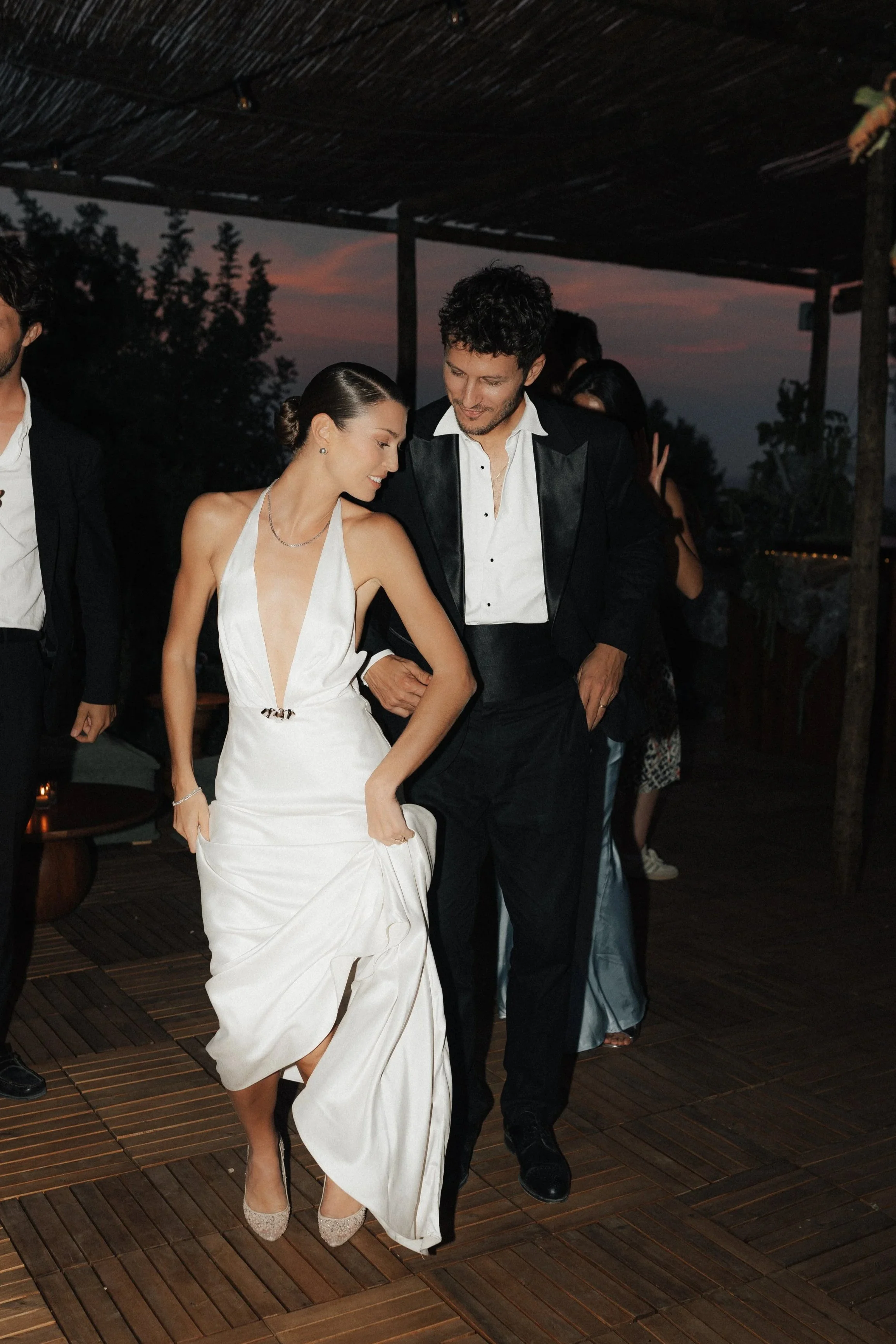 Ein Brautpaar beim Tanz bei einer Hochzeit im Freien bei Sonnenuntergang, die Frau trägt ein weißes Brautkleid, der Mann einen schwarzen Anzug.