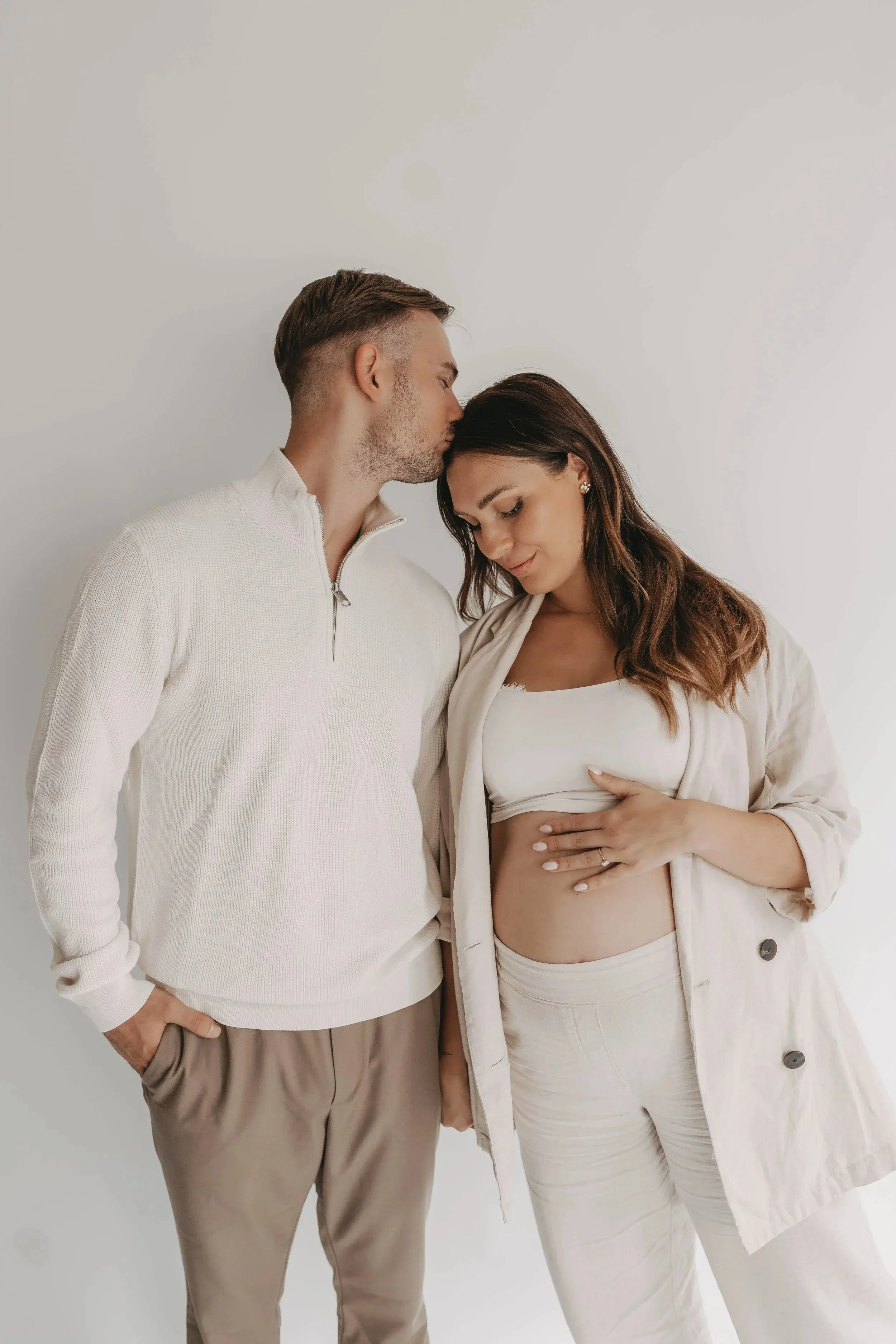 Ein verliebtes Paar, das eine schwangere Frau sanft berührt, vor einem weißen Hintergrund.