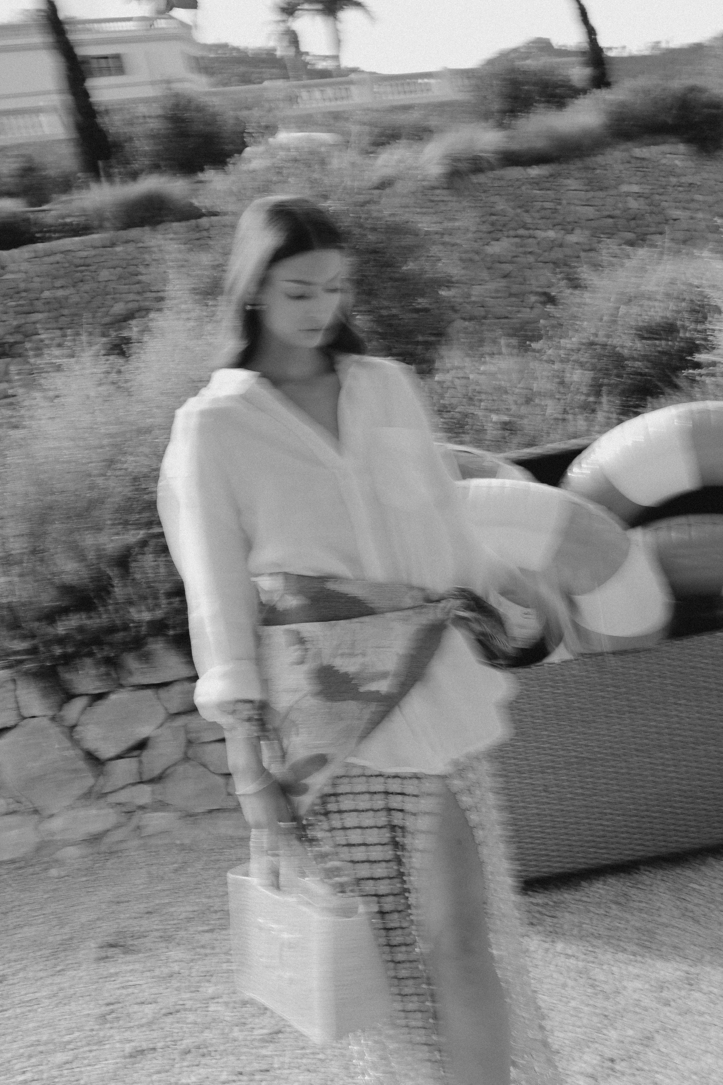 Schwarz-Weiß-Foto eines jungen Mädchens, das einen Kaffee hält, vor einer Steinmauer, mit einem aufblasbaren Reifen im Hintergrund.