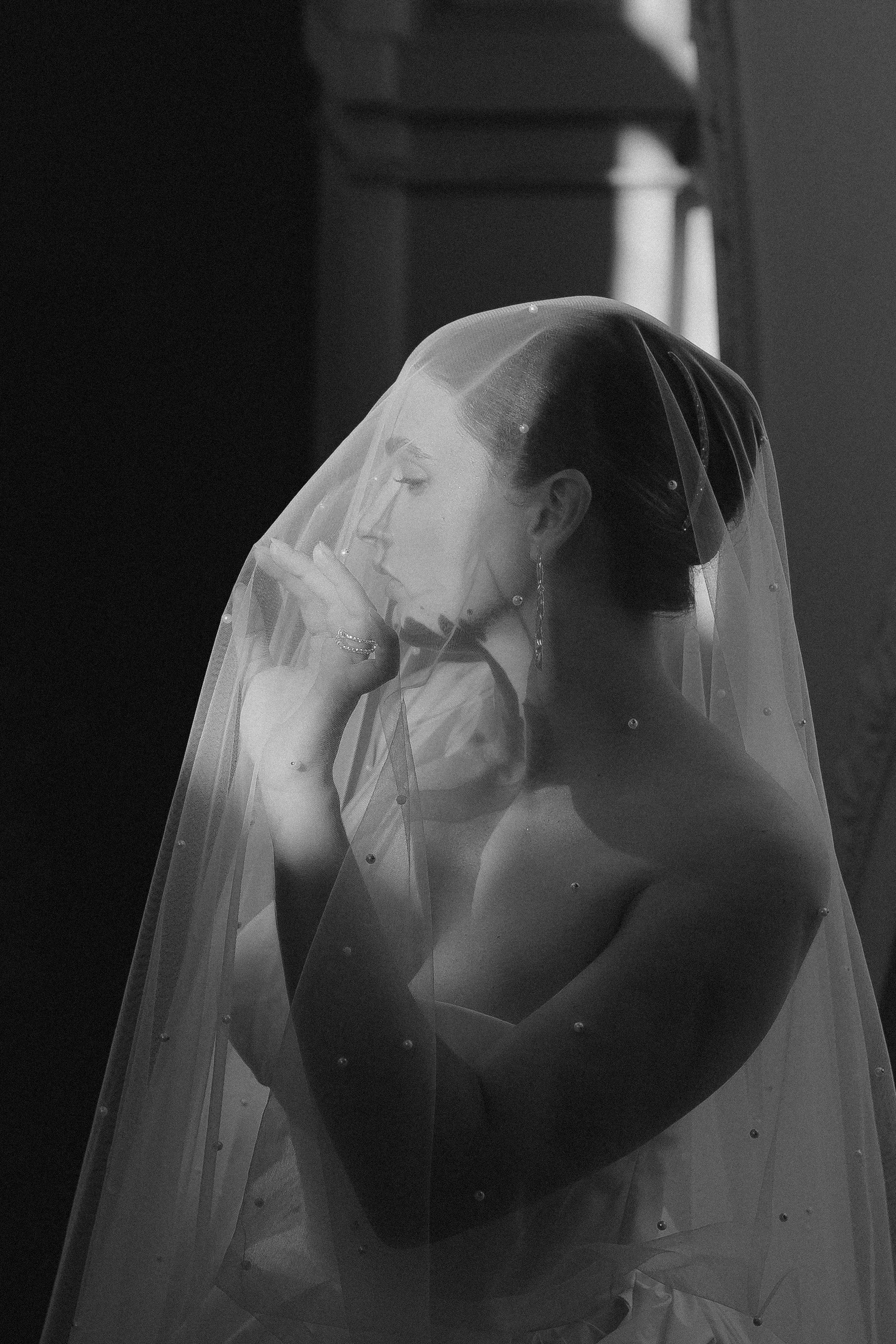 Schwarz-Weiß-Fotografie einer eleganten Frau im Hochzeitskleid mit Schleier, die nachdenklich wirkt.