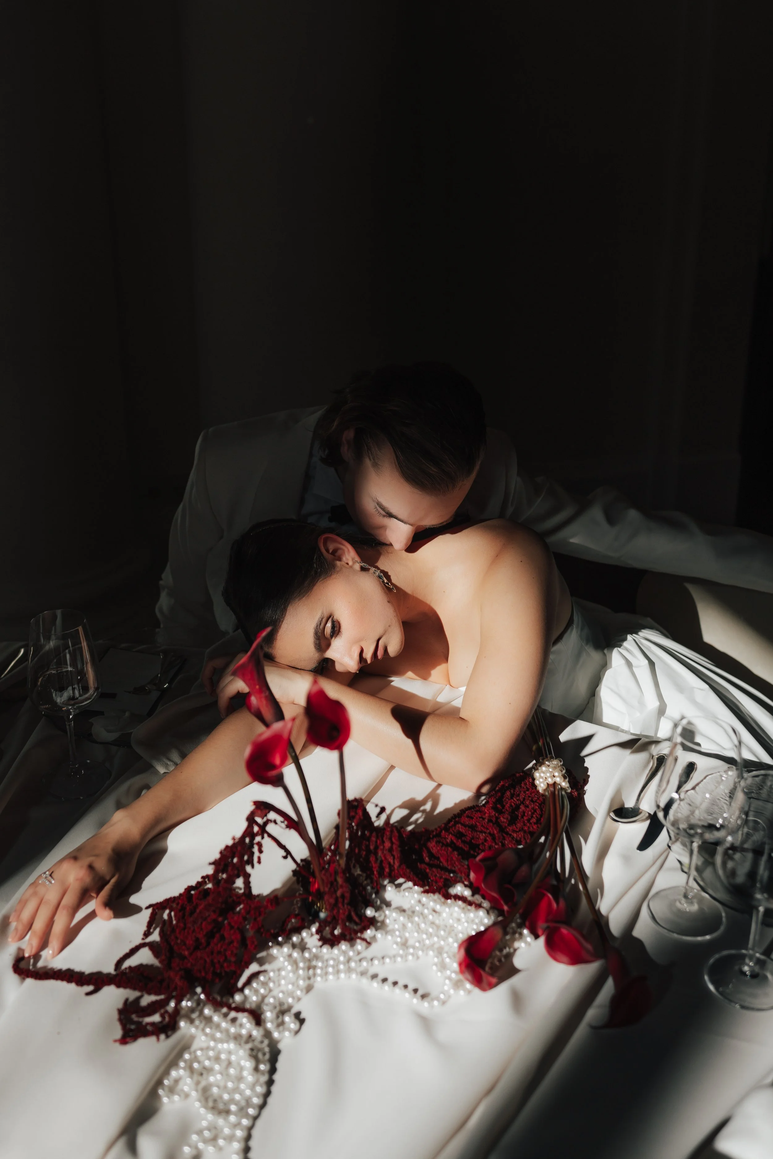 Zwei Frauen bei einer intimen Umarmung an einem festlich gedeckten Tisch, mit Blumen und Wein glasen, bei Dunkelheit.