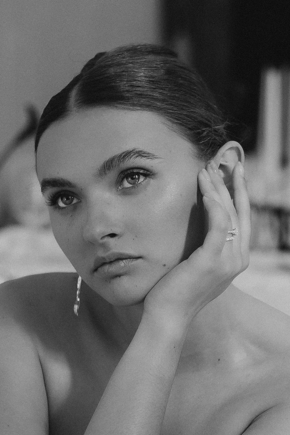 Schwarz-Weiß-Fotografie eines jungen Frauengesichts mit langen Haaren, die Hand an das Gesicht legt, Blick nach oben