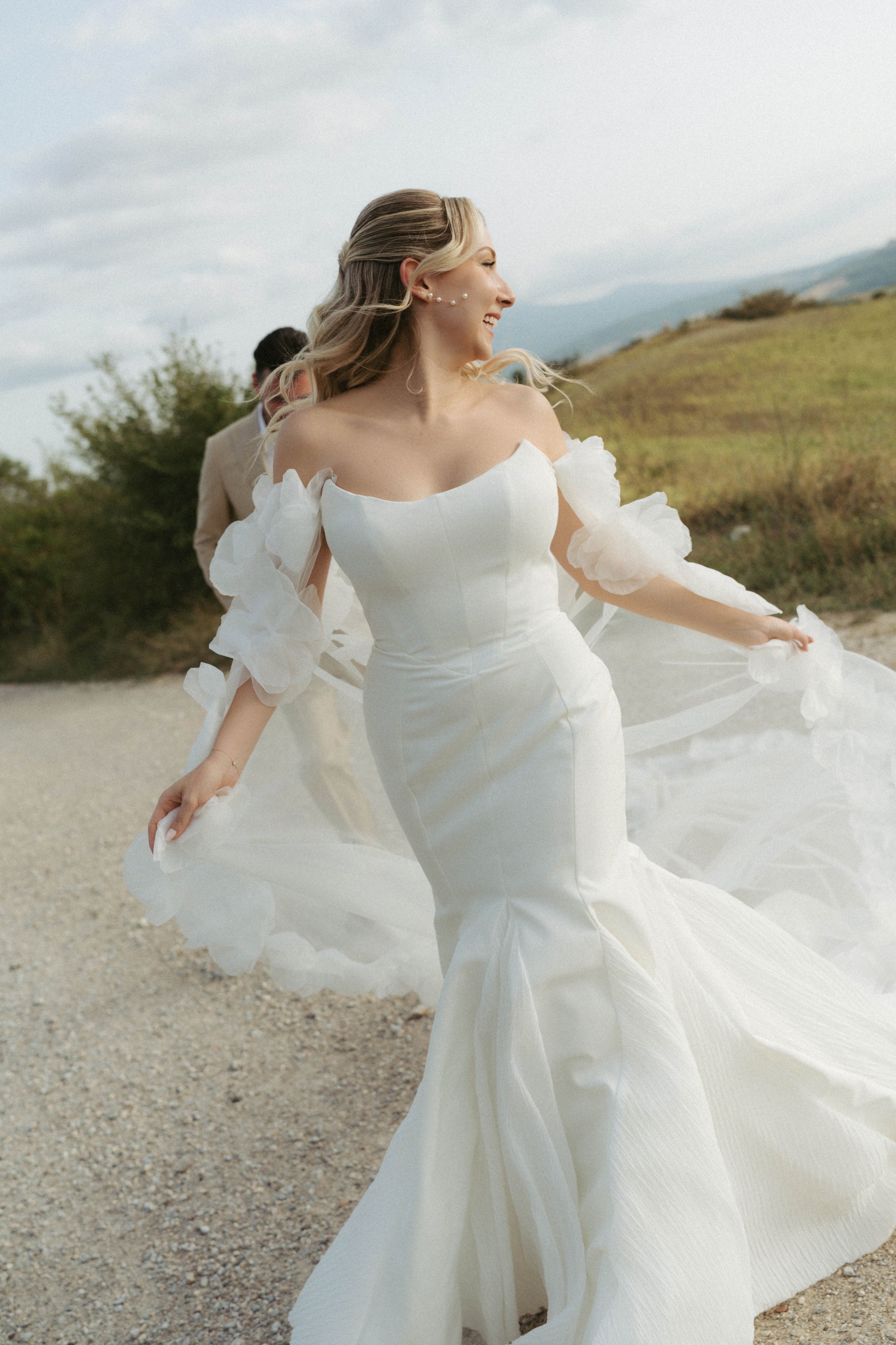 Freudige Braut in einem weißen Hochzeitskleid, die auf einer ländlichen Straße bei bewölktem Himmel läuft.