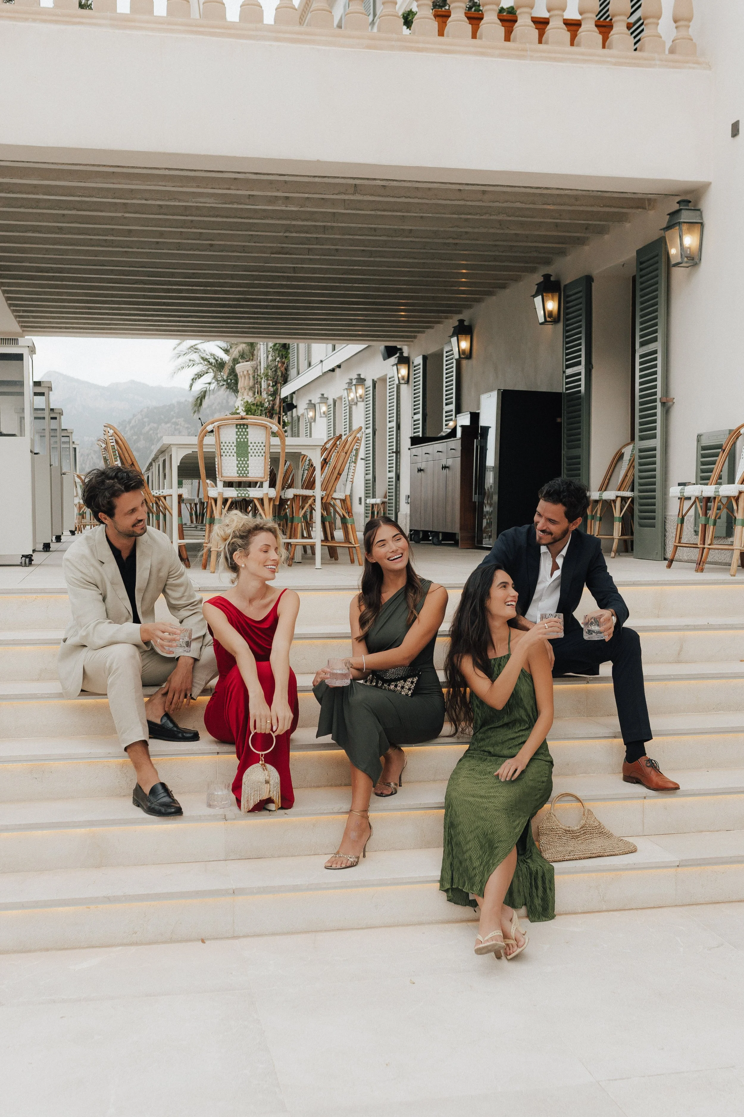 Eine Gruppe von fünf jungen Leuten sitzt entspannt auf Treppenstufen und lacht bei einem geselligen Treffen im Freien.