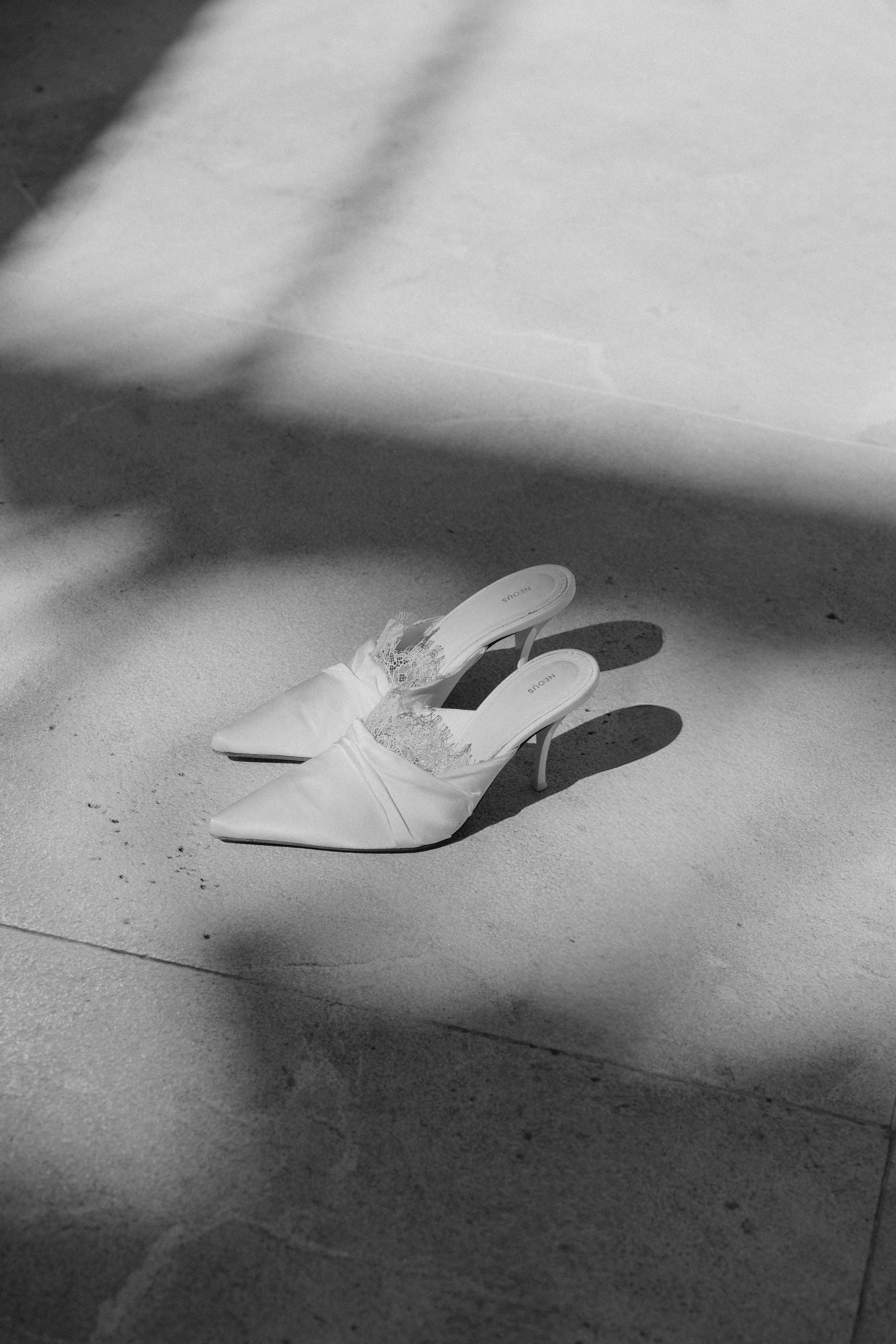 Weiße High-Heels mit Spitze auf einer glatten Bodenfläche, teilweise im Schatten.