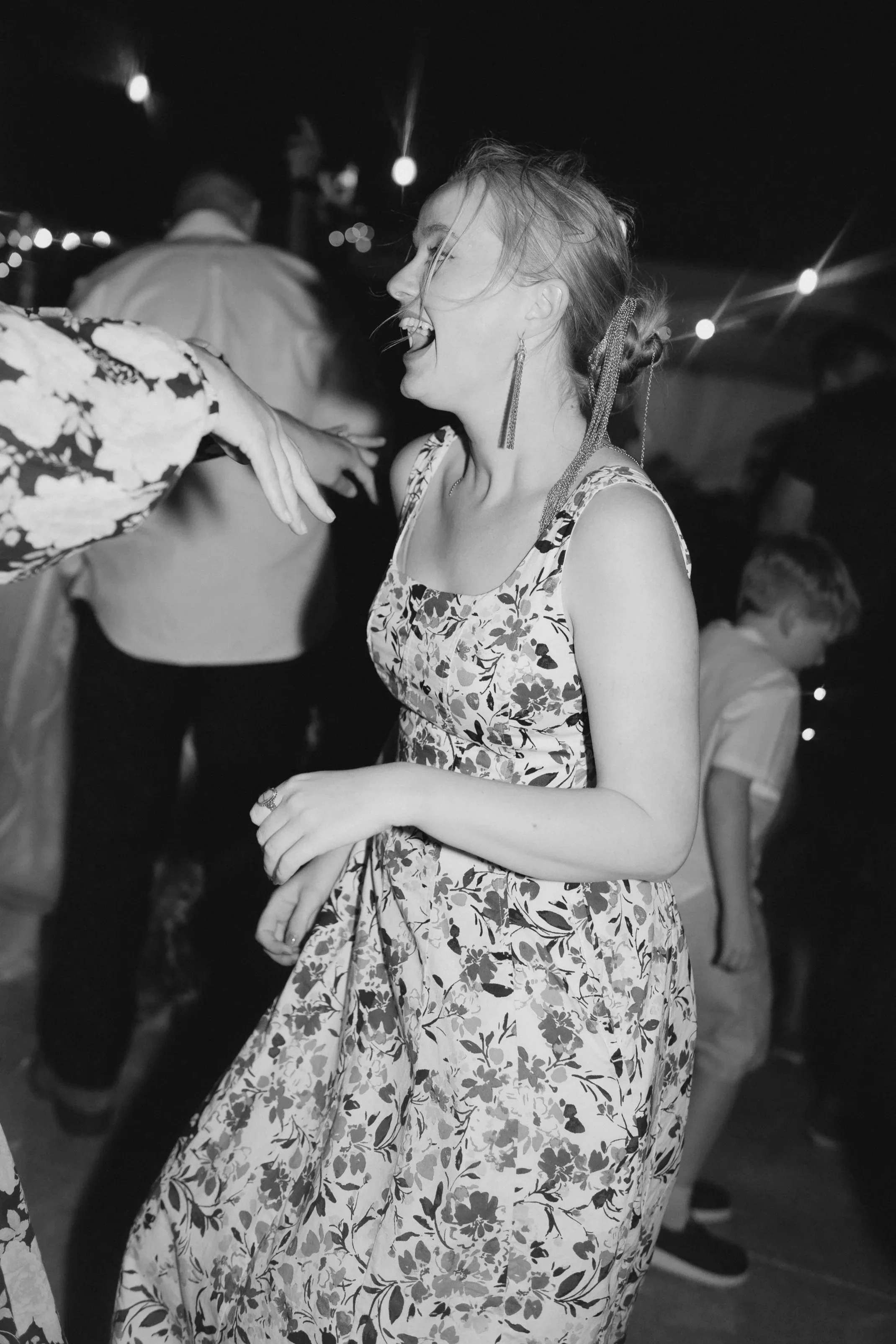 Frau in einem floral gemusterten Kleid tanzt bei einer Feier, während andere Personen im Hintergrund ebenfalls tanzen.