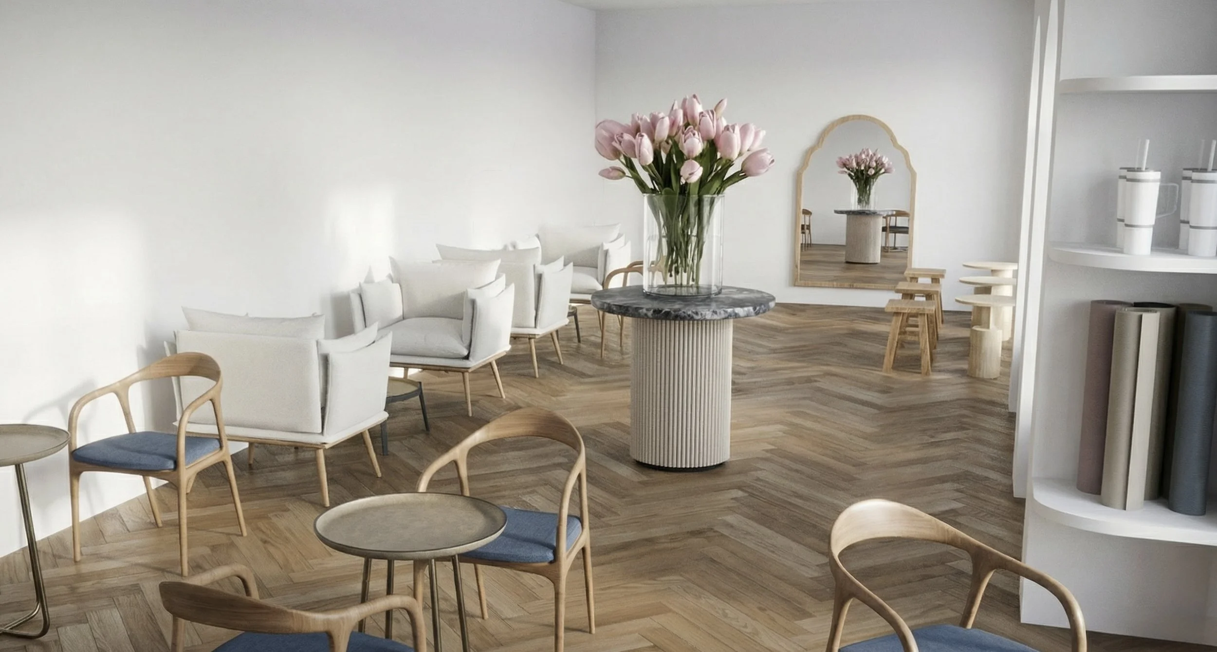 Interior of a modern cafe or lounge with wooden floors, white walls, a large mirror, white armchairs, wooden chairs with blue cushions, round tables, and a large vase with pink tulips on a round marble-top table.
