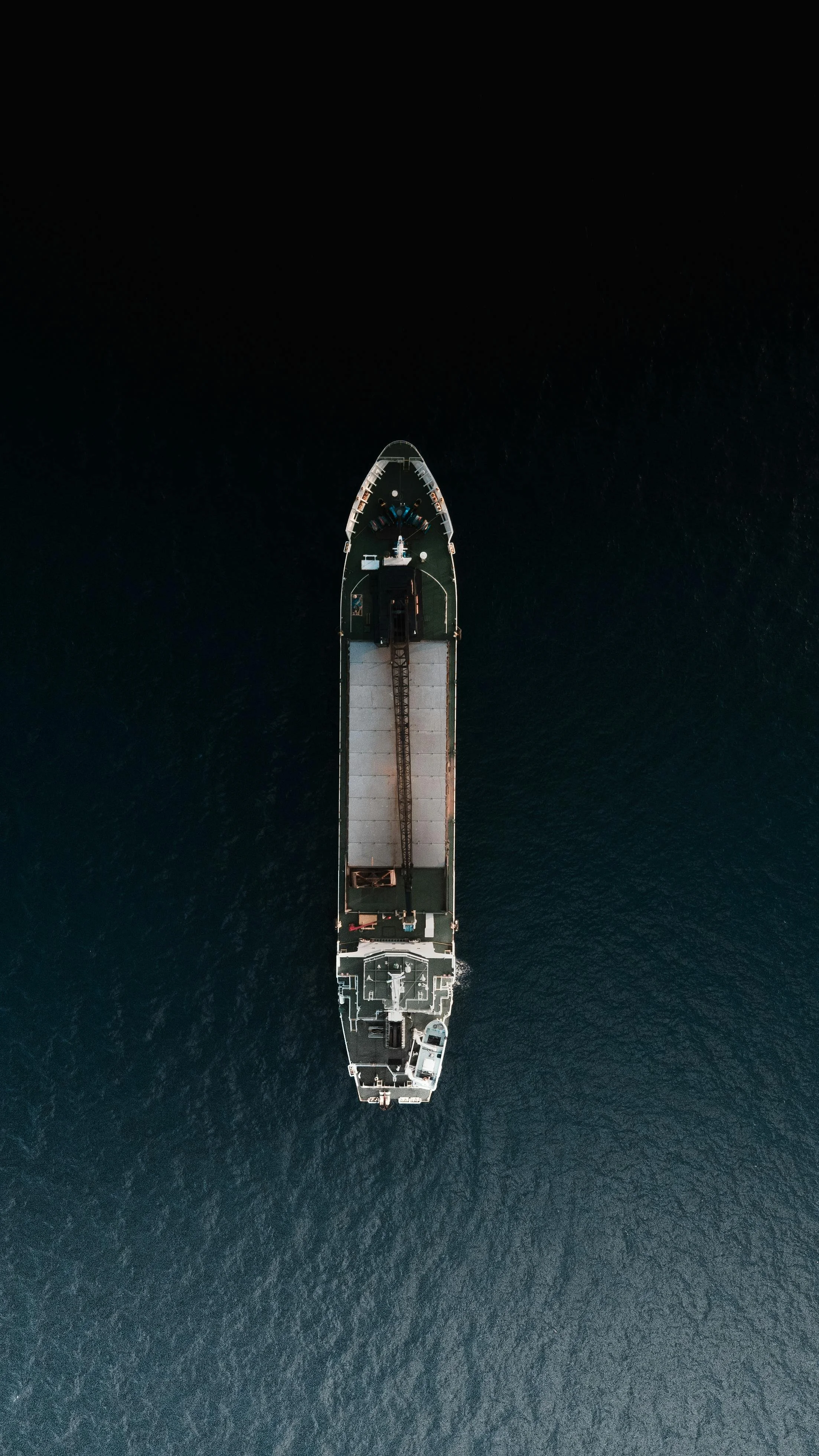 Top-down aerial view of a large cargo ship sailing in dark blue water.
