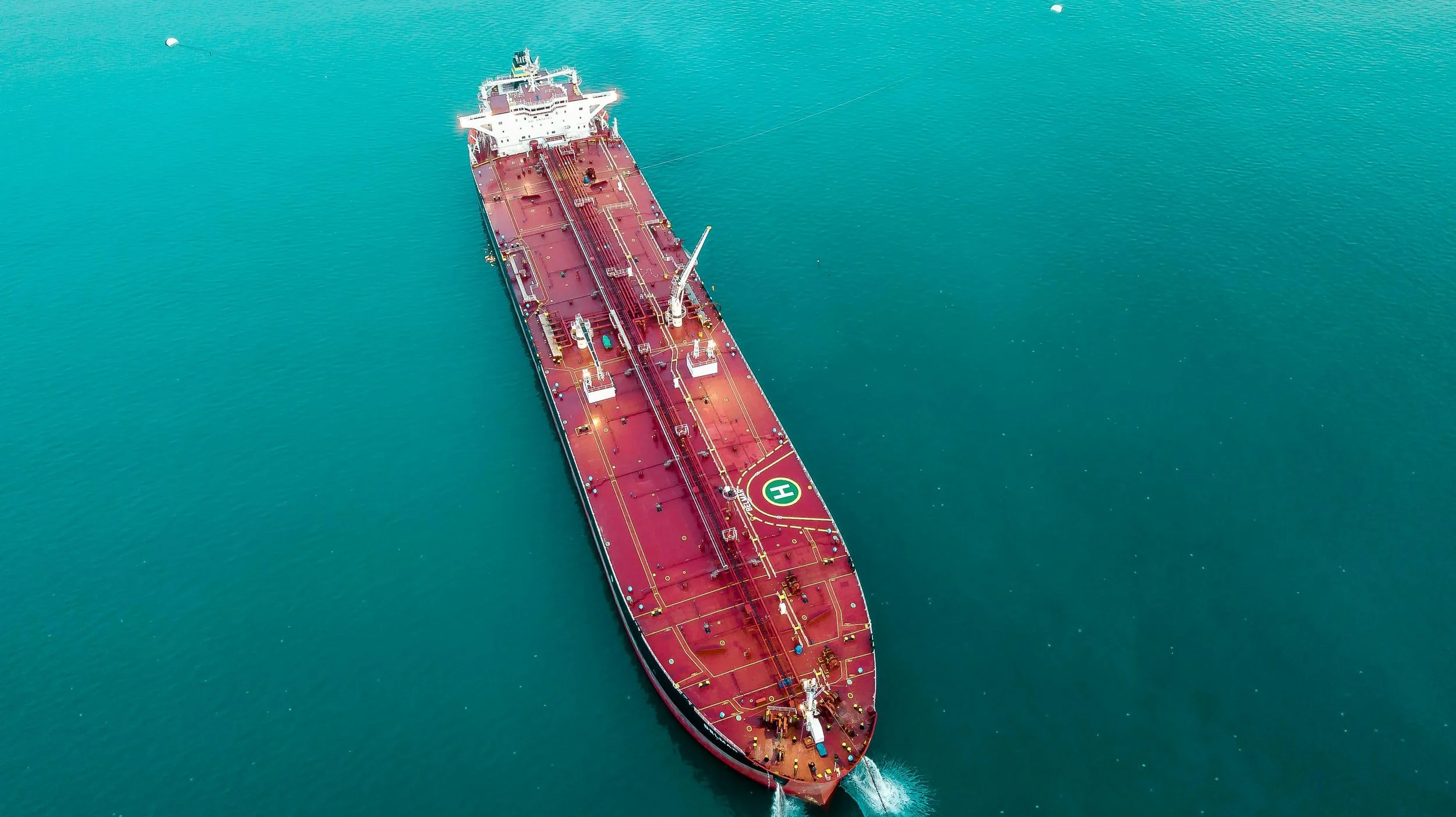 An aerial view of a large red oil tanker ship sailing on calm blue water.