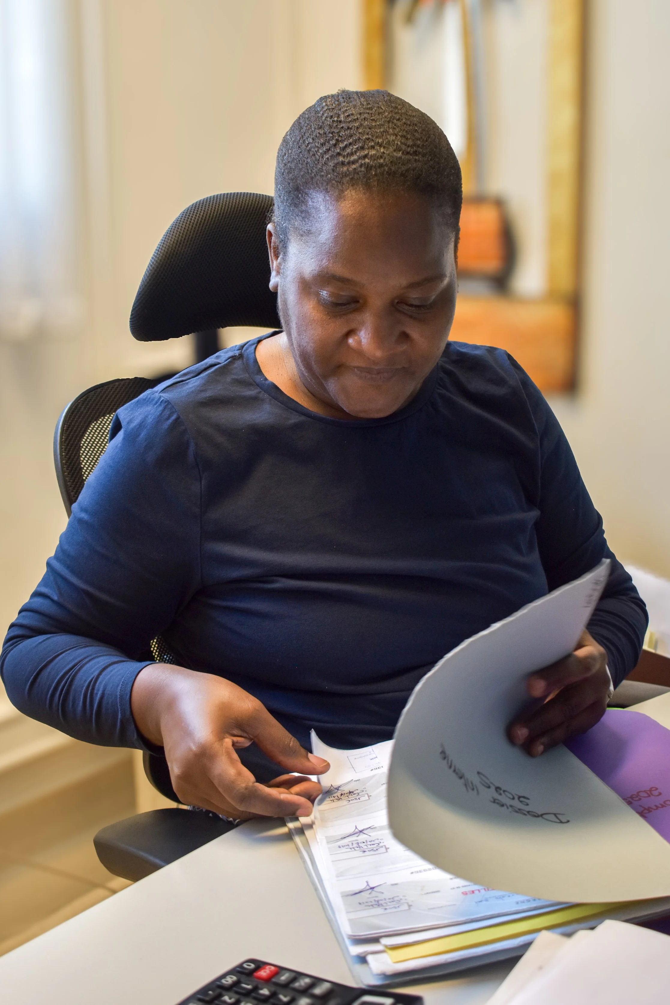 Une femme regarde des documents sur un bureau, à l'intérieur en arrière-plan.