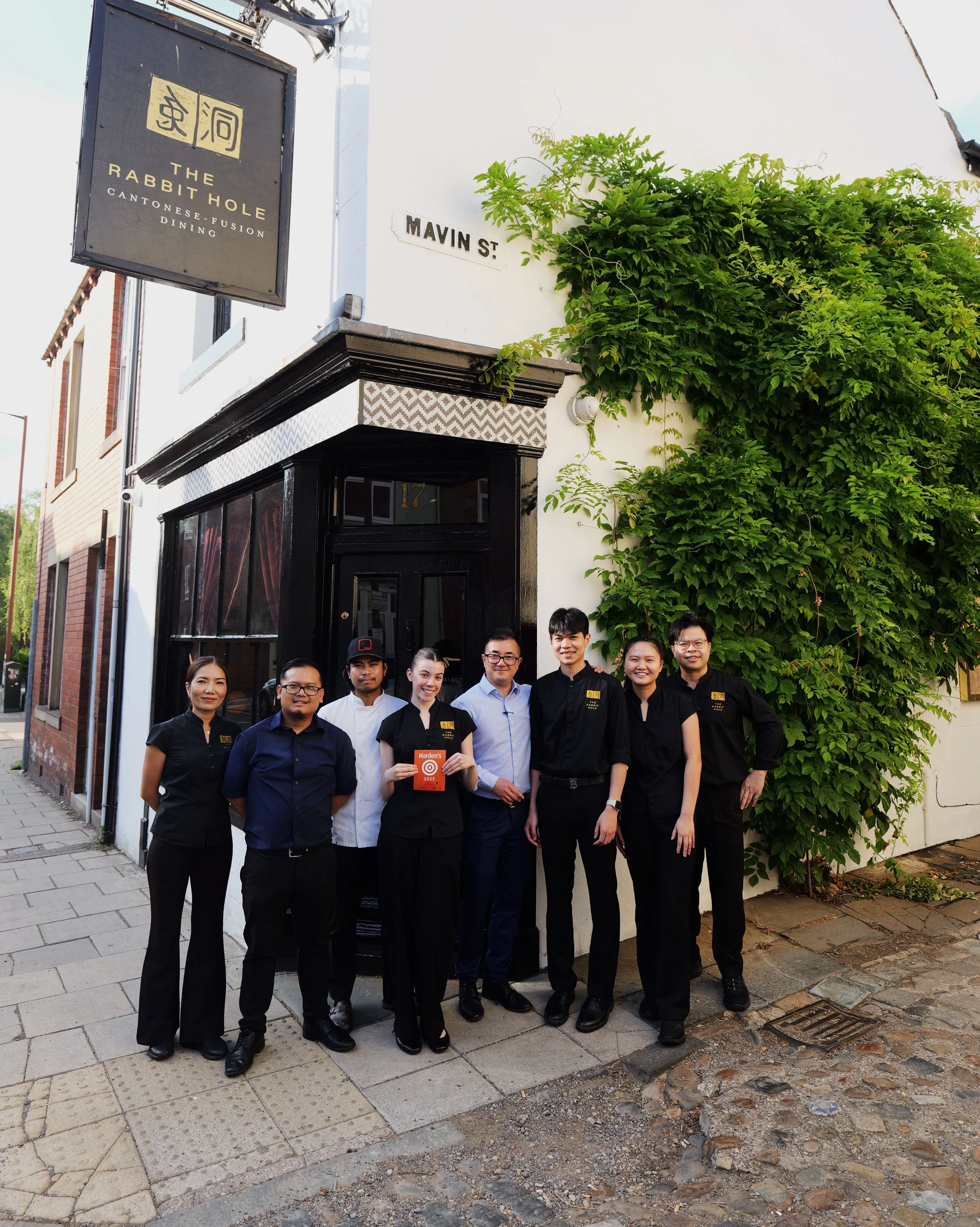 Group of seven staff members standing outside a restaurant called The Rabbit Hole on Mavin Street, smiling for the photo, with greenery and a building in the background.
