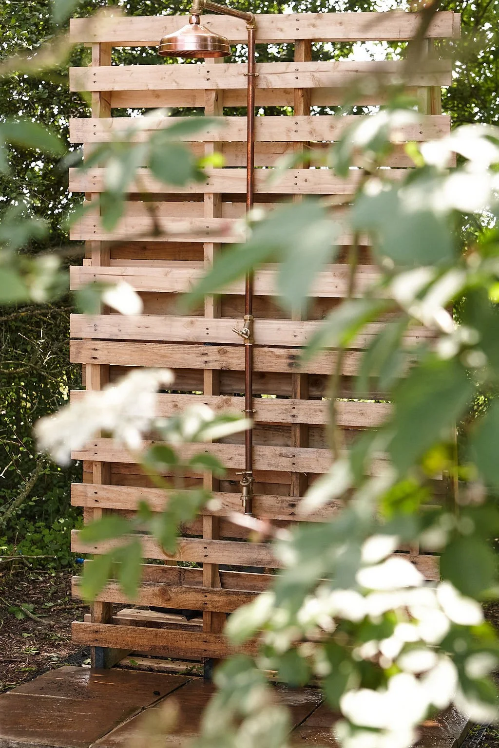 Outdoor copper shower with wooden screen and greenery