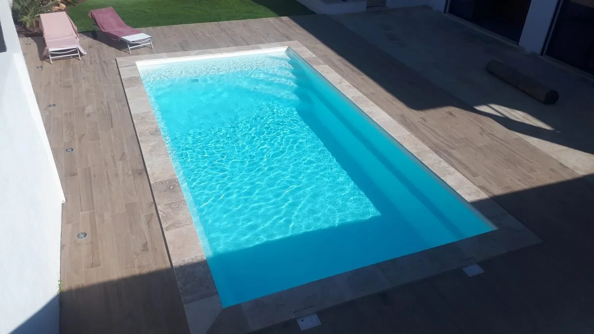 Piscine coque Generation Piscines à l'eau turquoise, bordée de margelles et d'une plage en bois