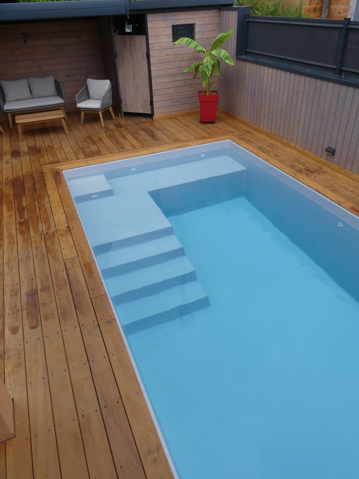 Piscine coque avec escalier d'angle, entourée d'une terrasse en bois