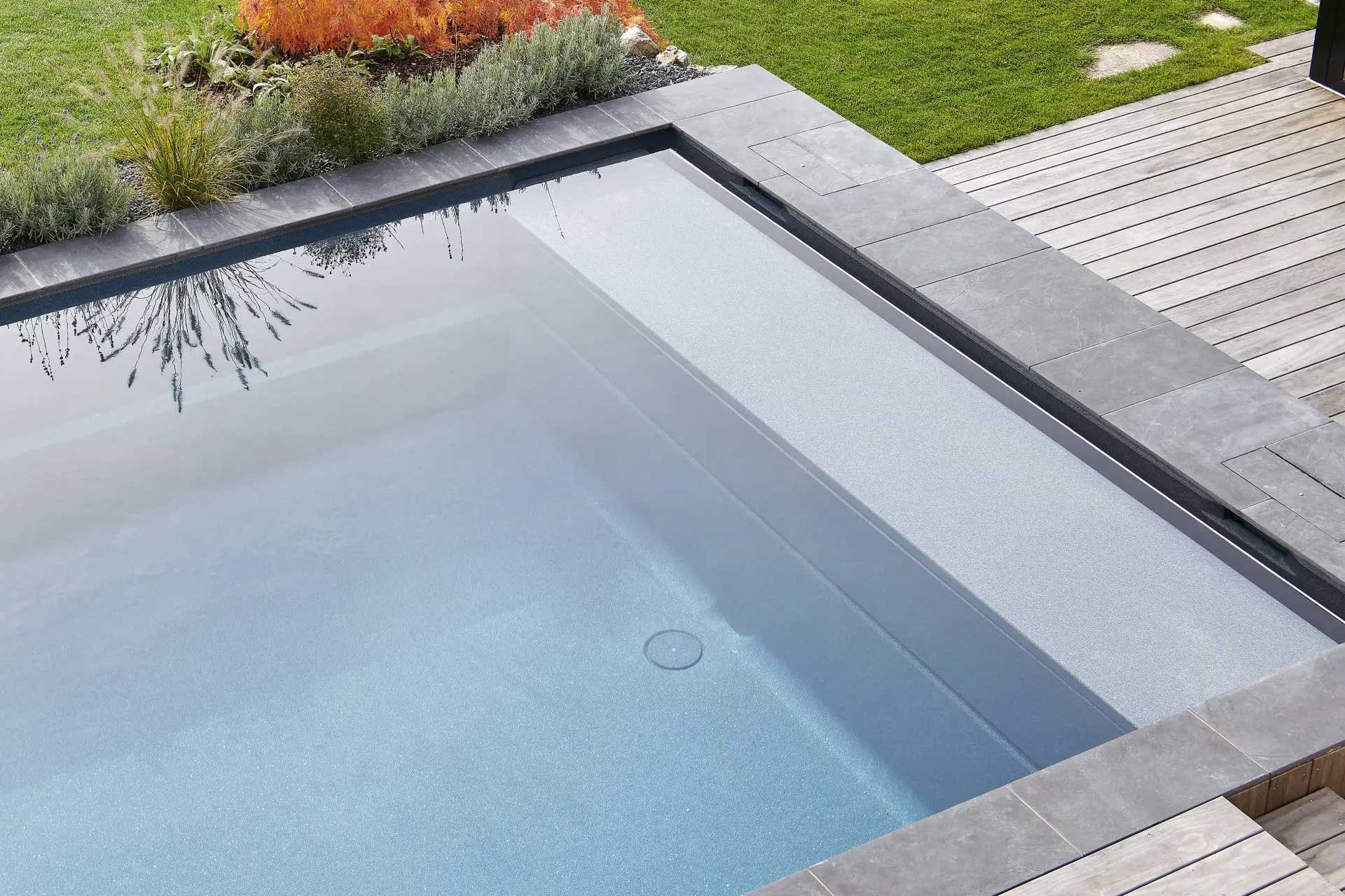 Angle d'une piscine coque à l'eau claire, bordée de margelles grises et d'une terrasse bois