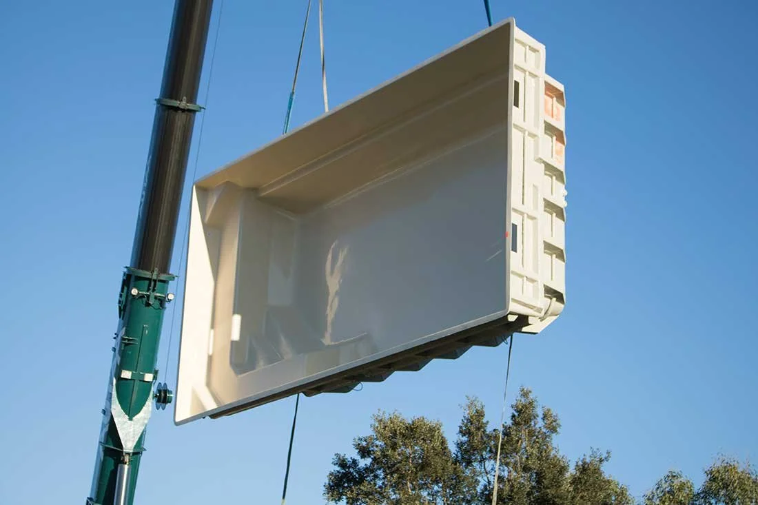 Coque de piscine soulevée par une grue lors de sa livraison sur le chantier