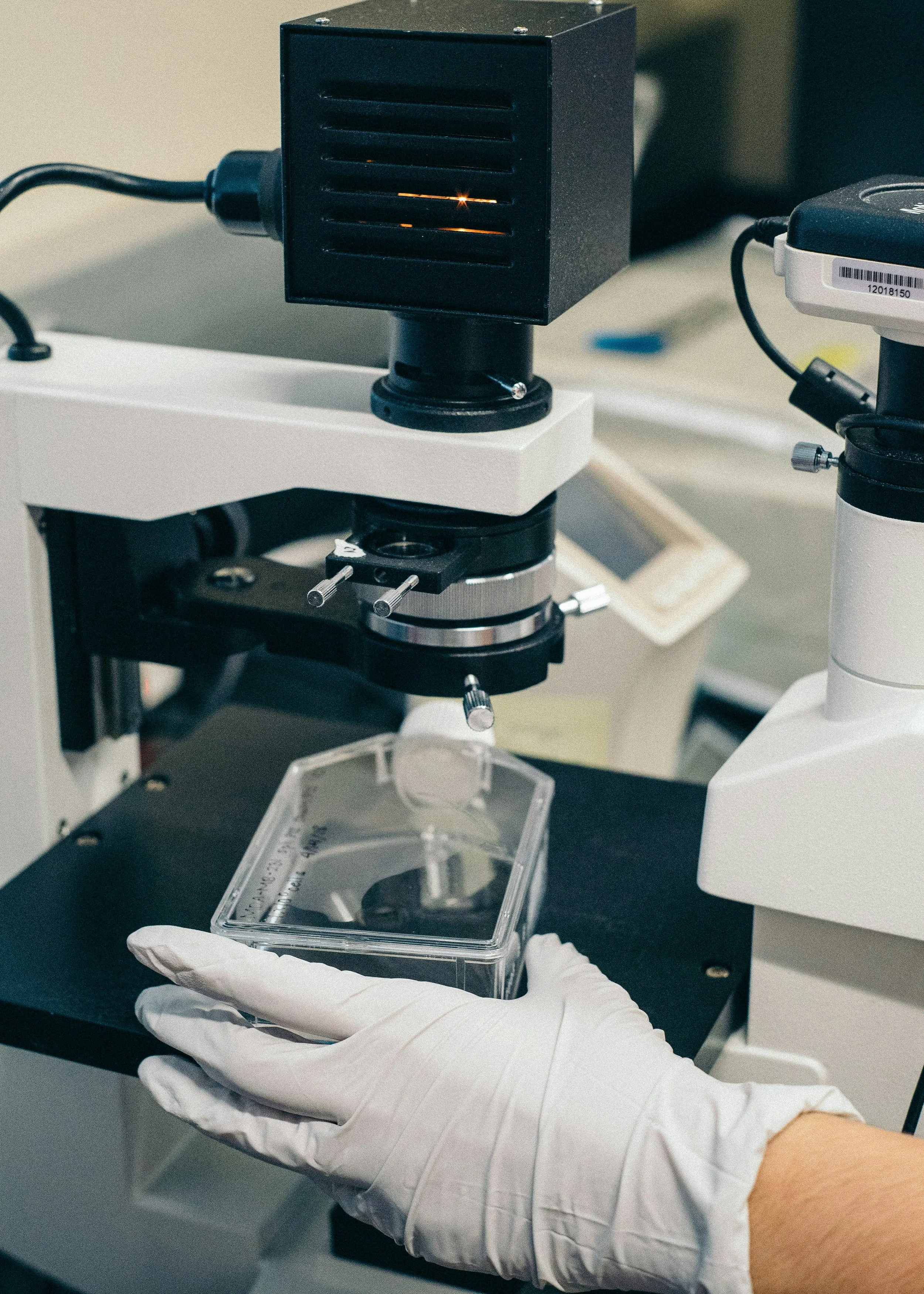 Stock photo of a black and gray laboratory instrument, slide, and gloved hand. Source: Unsplash/Jaron Nix.