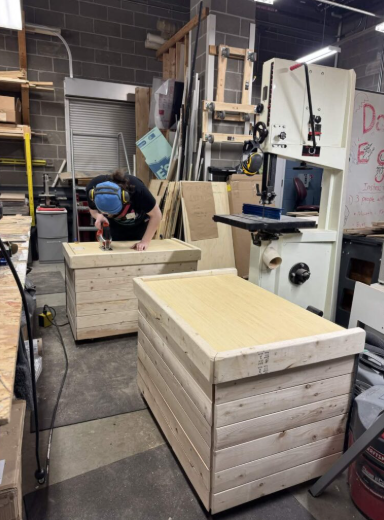 Photo of the Remnants team fabricating the wooden flower boxes in the woodshop. A team member is working with tools to create the four boxes. Photo: Remnants Team.
