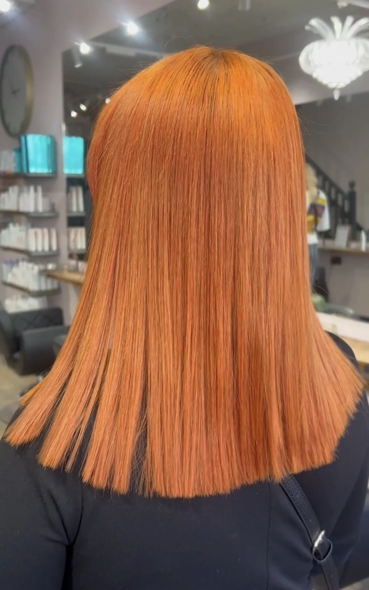 A person with straight, shoulder-length, bright orange hair in a salon.