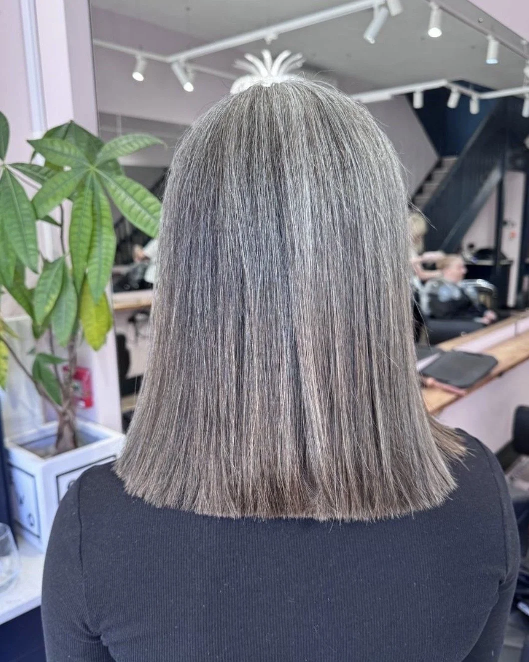Back view of a person with straight, shoulder-length gray hair in a hair salon.